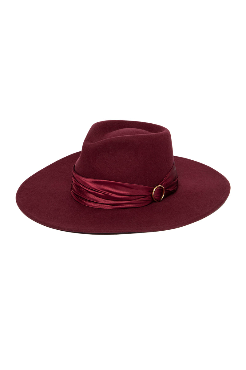 The Tt Josie Wool Felt Fedora in red features a wide brim, matching satin band, and gold buckle detail around the crown, set against a white background—a true statement piece among luxury accessories.