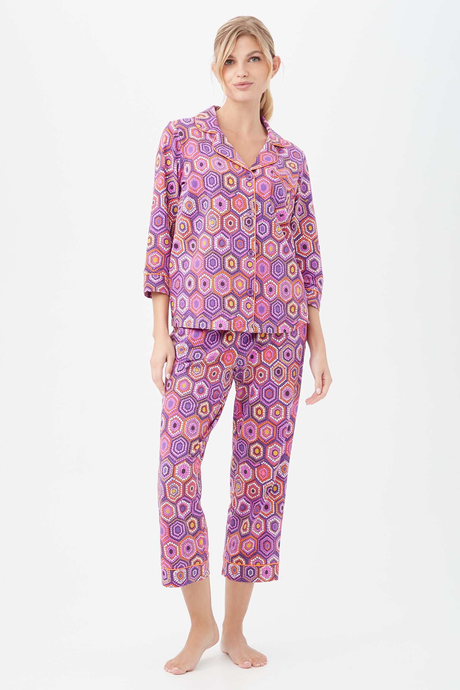 A woman stands barefoot in the Honeycomb Dots Womens 3/4-Sleeve Cropped Pant Jersey PJ Set, featuring a colorful geometric hexagon pattern, against a plain white background.