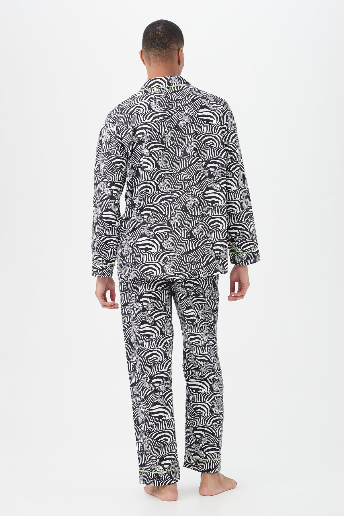 A person stands barefoot with their back to the camera, modeling the Zebra Safari Mens Long Sleeve Long Pant Poplin PJ Set with a bold black and white zebra pattern. The lightweight pajamas contrast against a plain white background.