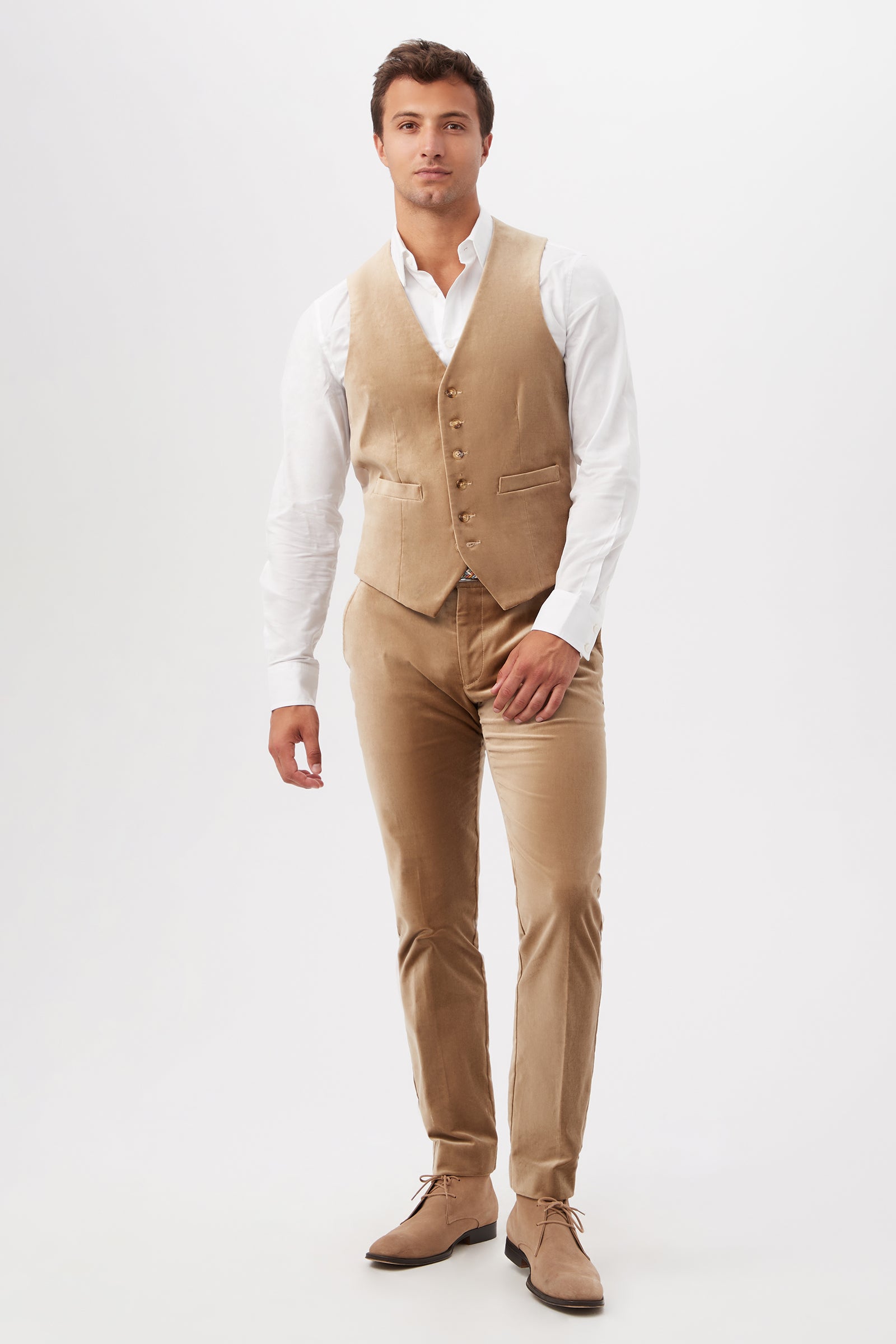 A man stands against a plain white background wearing the Irving Vest in Gold Velveteen, matching trousers, a white dress shirt, and tan dress shoes. He looks forward with a neutral expression and relaxed posture.
