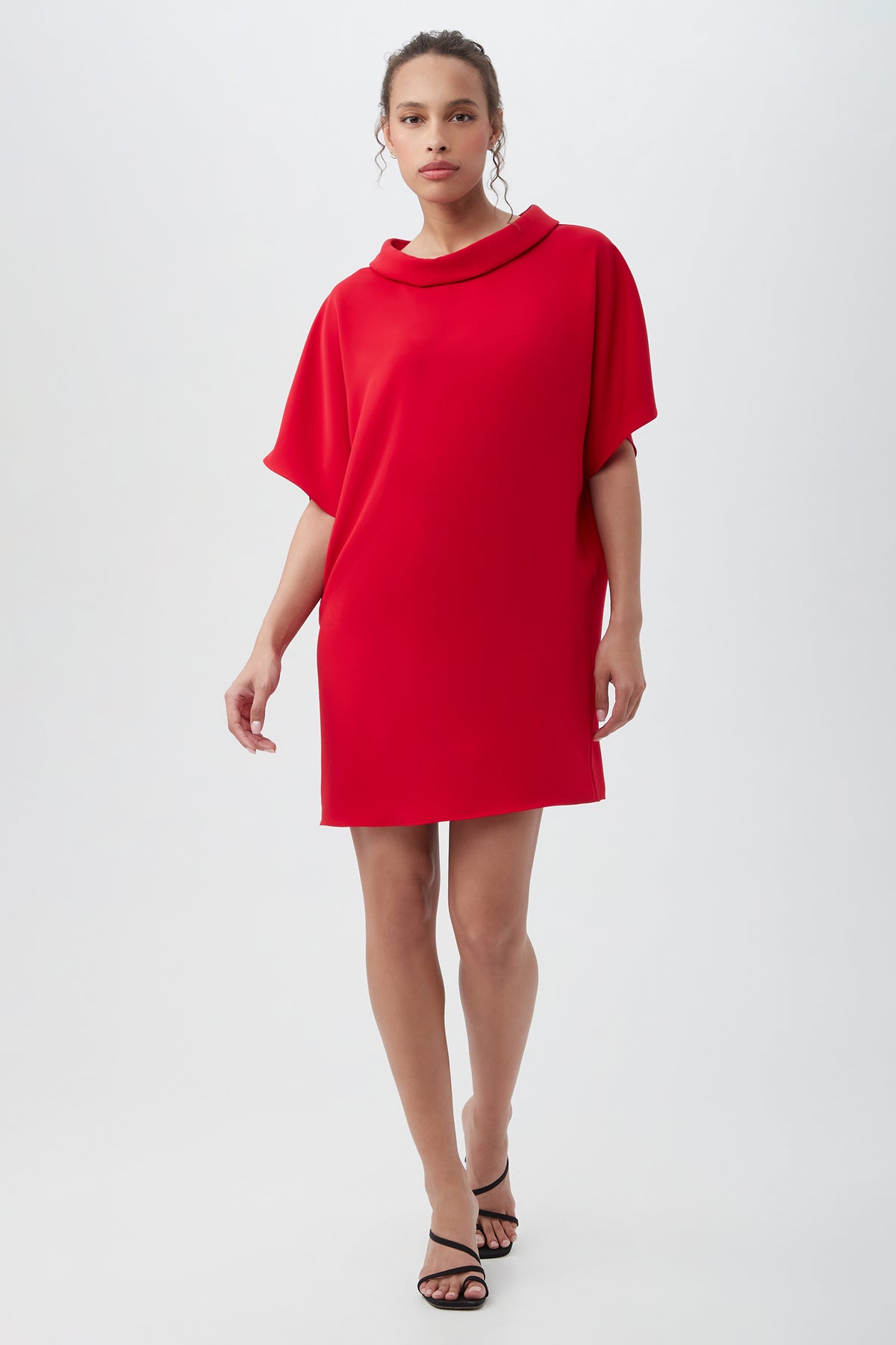 A woman wearing the Honeysuckle Short Dolman Sleeve Shift Dress in Red Spark stands against a plain white background, styled with black heeled sandals.