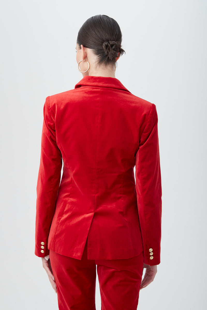 A person with dark hair in a low bun is photographed from behind against a plain light background, wearing the Midlands Velveteen Blazer Jacket and large hoop earrings.