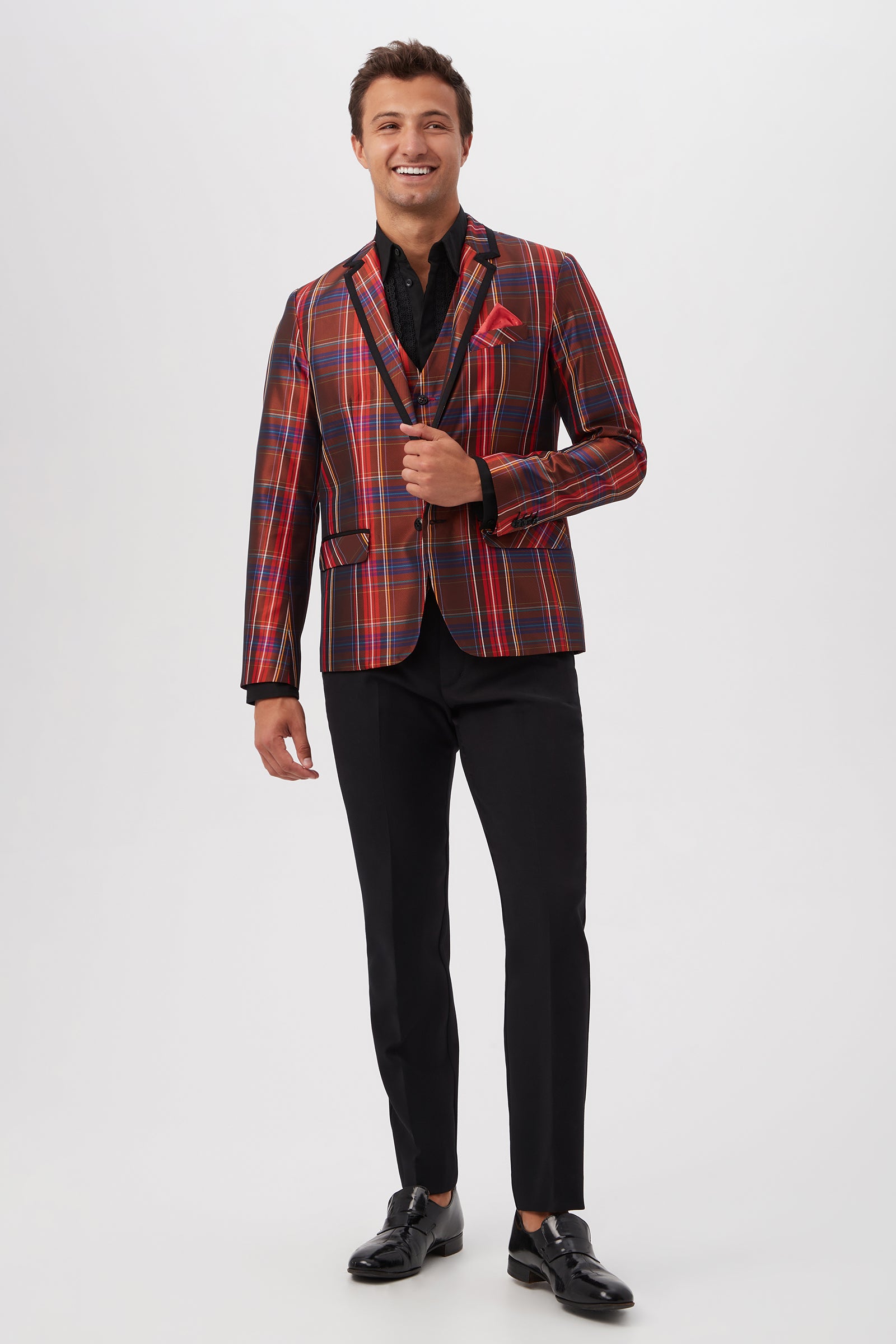 A smiling man stands against a plain white background wearing black Alex Slim Trouser - Luxe Drape with a red and gold plaid blazer, black shirt, and black dress shoes.