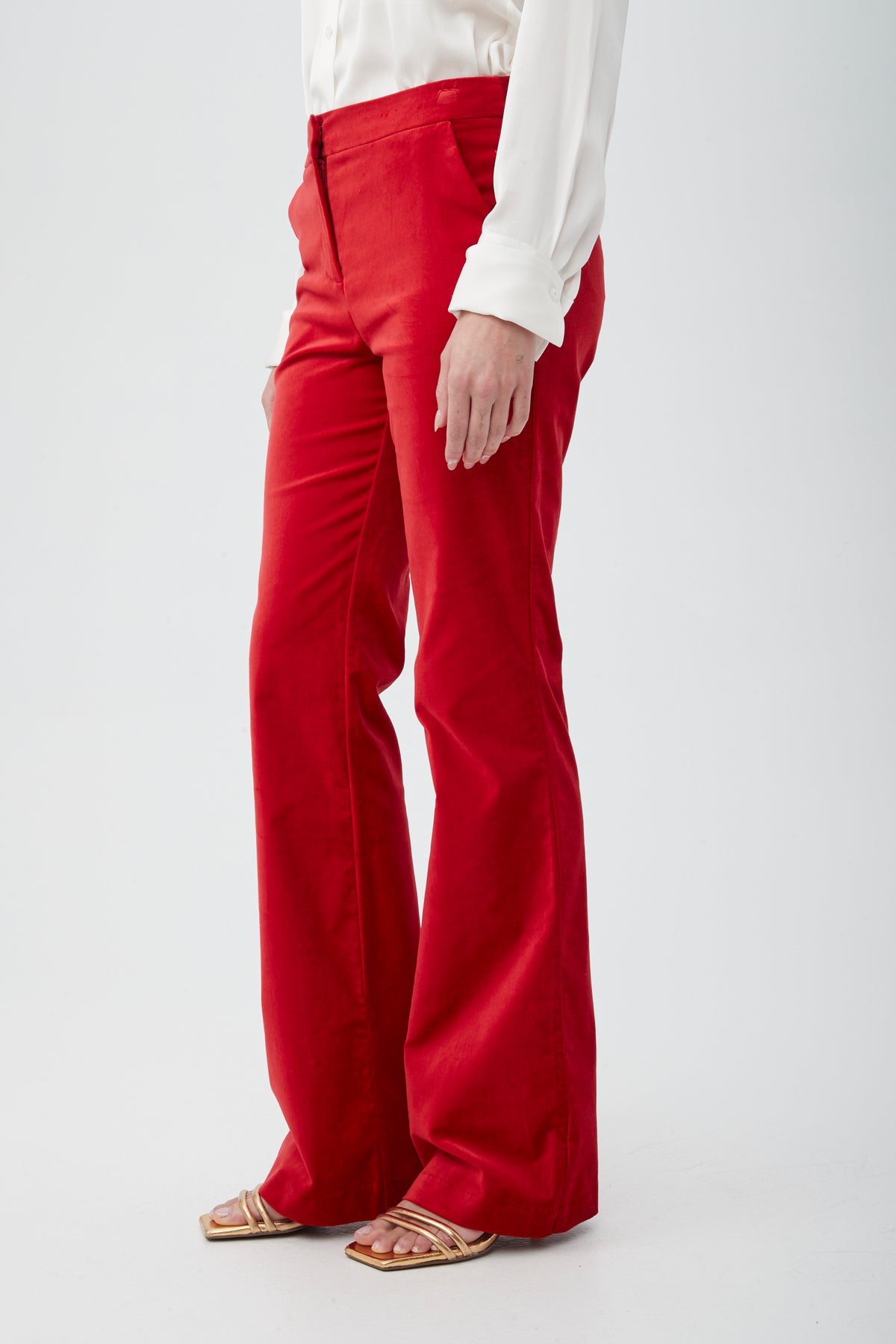A person models the Westport Velveteen Bootcut Pant in bright red, paired with a white long-sleeve blouse and gold open-toe sandals against a plain white background. Only their lower body is visible.