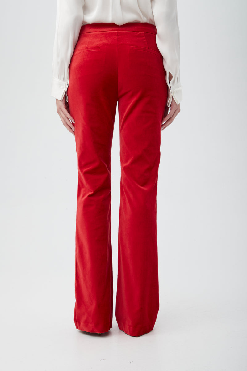 A person stands facing away against a plain white background, wearing the Westport Velveteen Bootcut Pant in bright red and a long-sleeve white shirt.