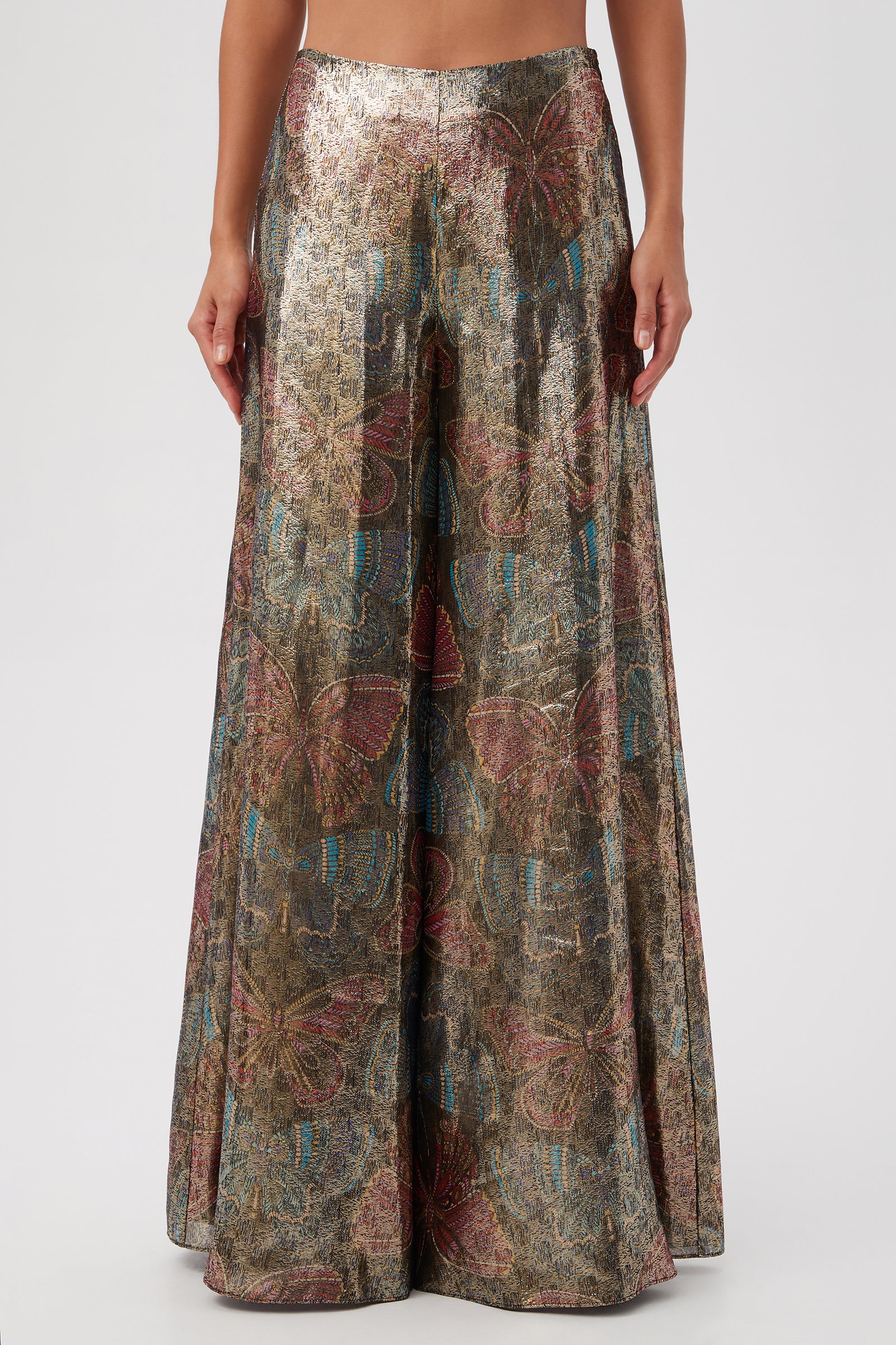 A person wearing Siya Butterfly Print Silk Wide Leg Pant, featuring a high-waisted fit and a colorful metallic butterfly pattern in gold, pink, and blue, stands against a plain background.