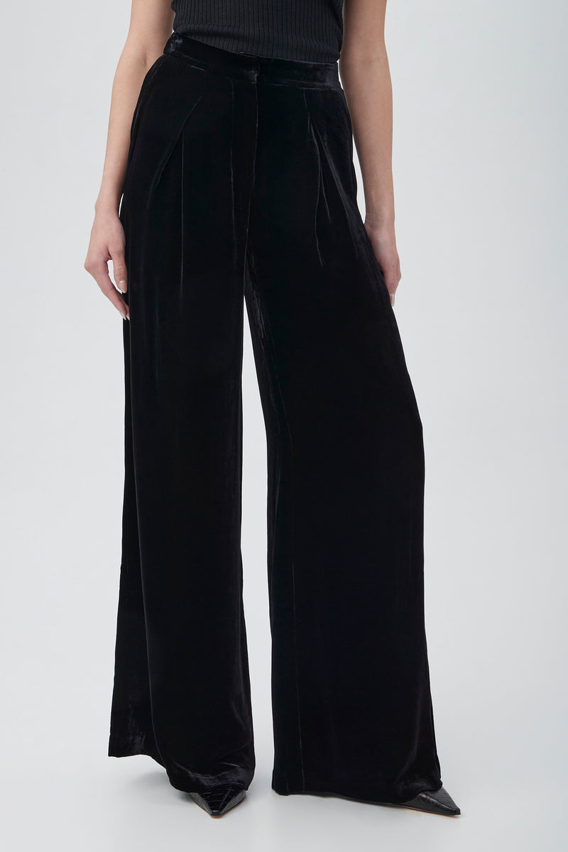 A model showcases the Saige Velvet Wide Leg Pants in BLACK, standing against a plain light gray background. The head and upper torso are out of frame.
