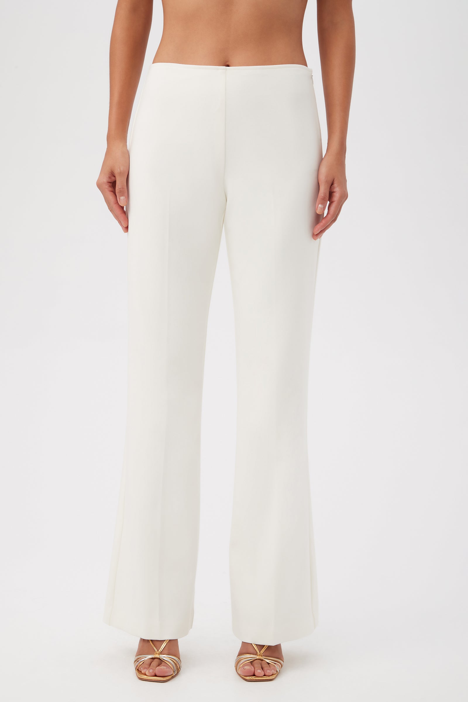 A person wears the Lancelot 2 Luxe Drape Bootcut Pants, featuring a high-waisted, white, wide-leg silhouette with gold open-toe heels. The photo is cropped from shoulders down against a plain white background.