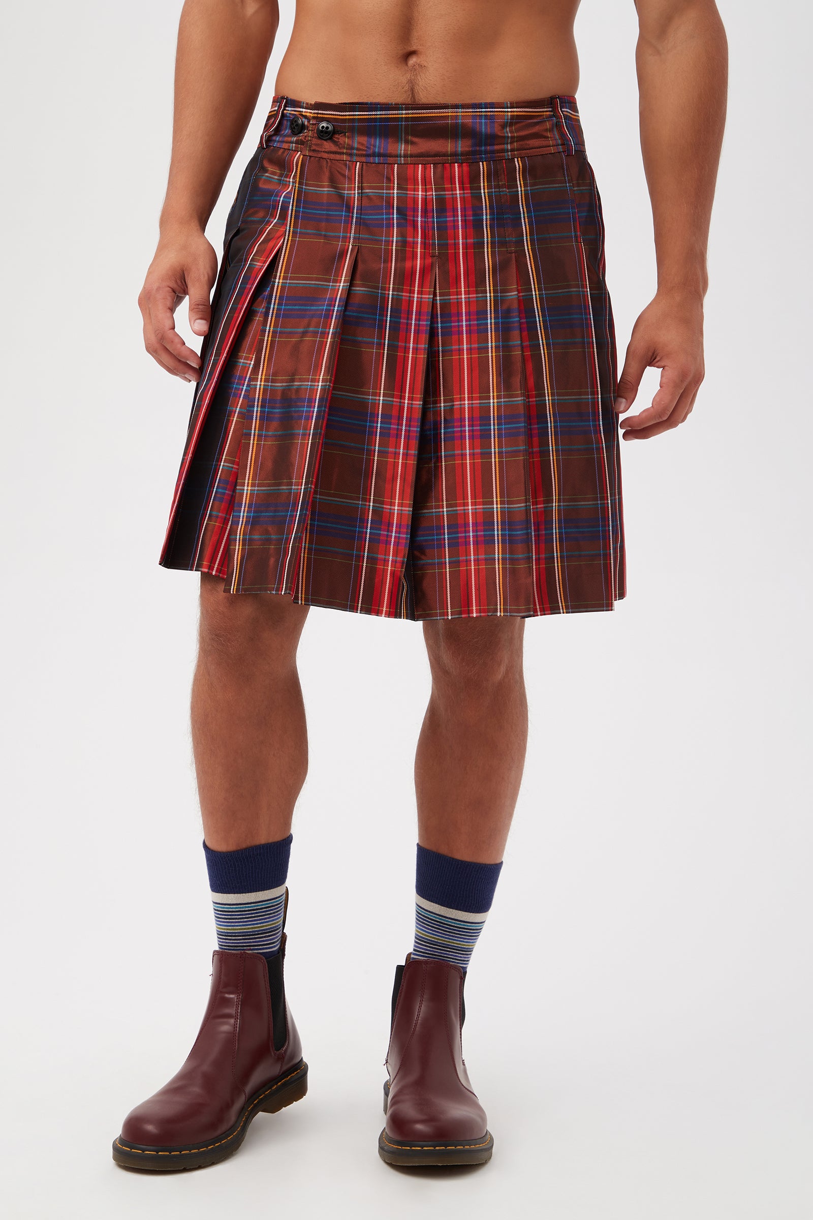 A person wears the Livingston Pleated Kilt - Plaid Taffeta (Multi) with blue and gray striped socks and brown ankle boots. The cropped photo shows their body from shoulders to feet against a plain white background.