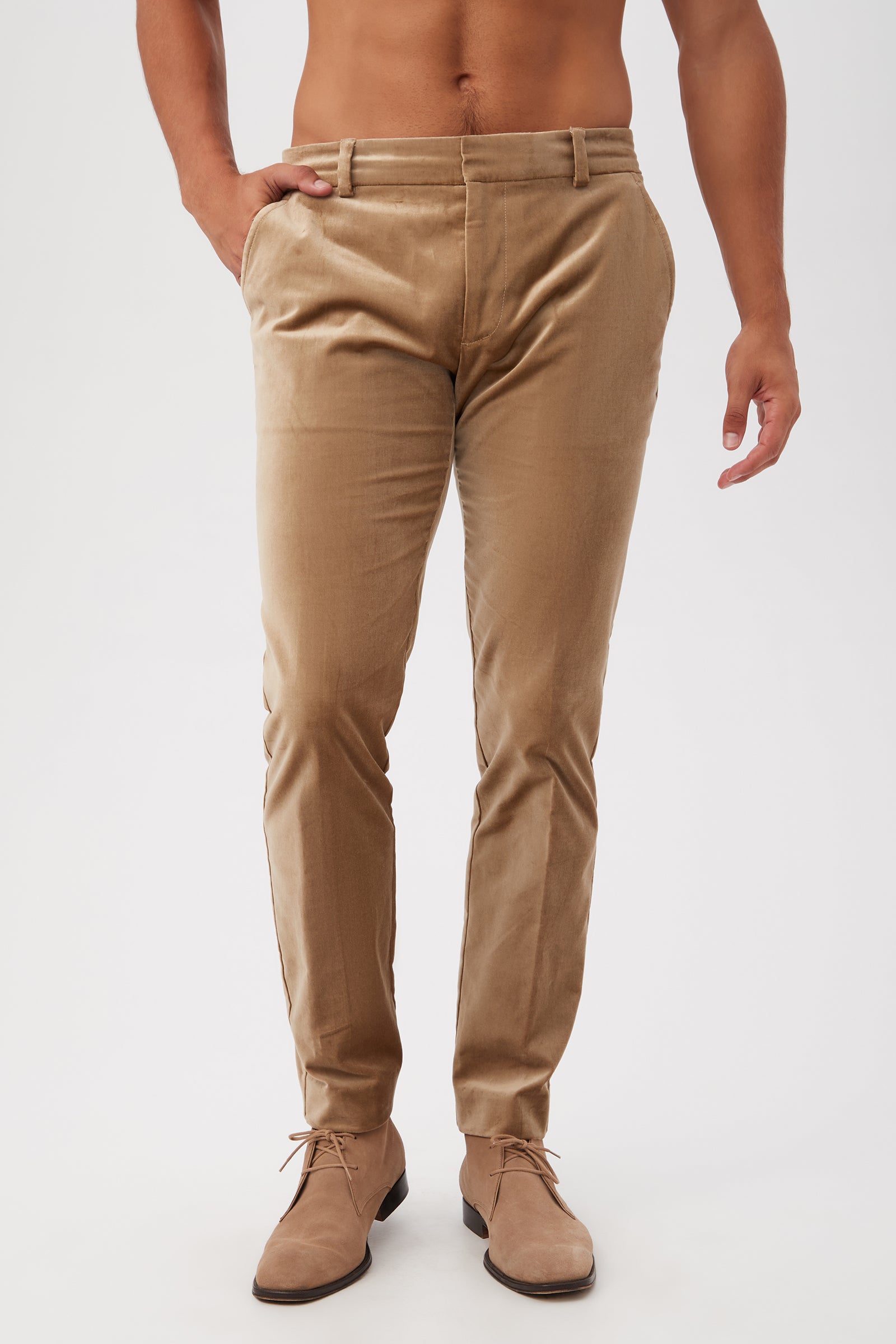 A shirtless man wearing the Clyde Slim Trouser in gold velveteen stands with one hand in his pocket against a plain white background.