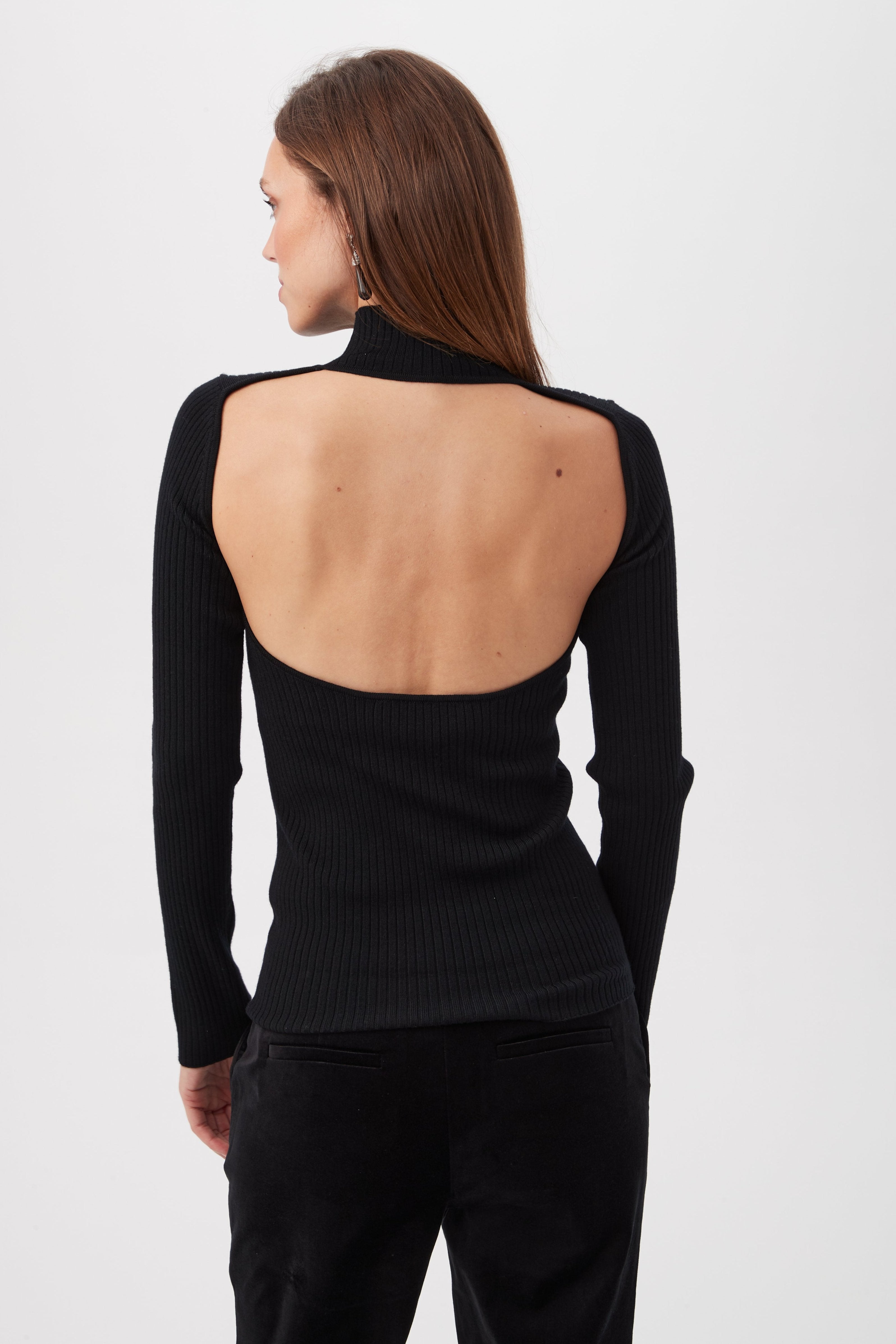 A woman wearing the Sade Merino Wool Mockneck Sweater with an open back stands with her back to the camera against a plain white background.