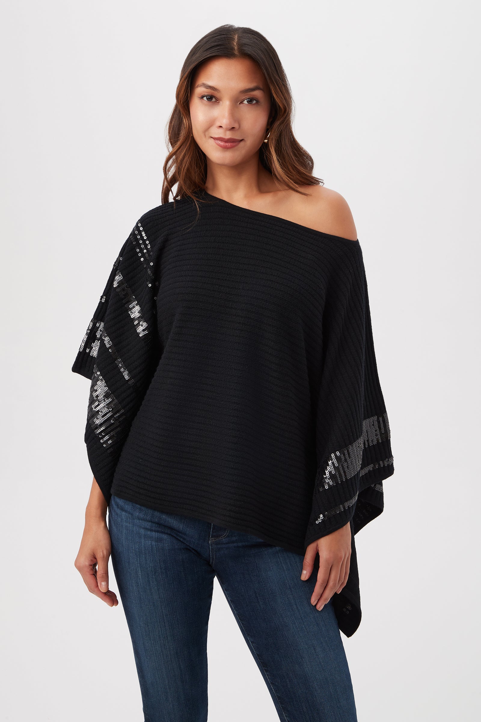 Woman with long brown hair wearing the Adela Merino Wool Wrap Sweater With Black Sequin Stripes and blue jeans, standing against a plain white background, looking at the camera with a neutral expression.