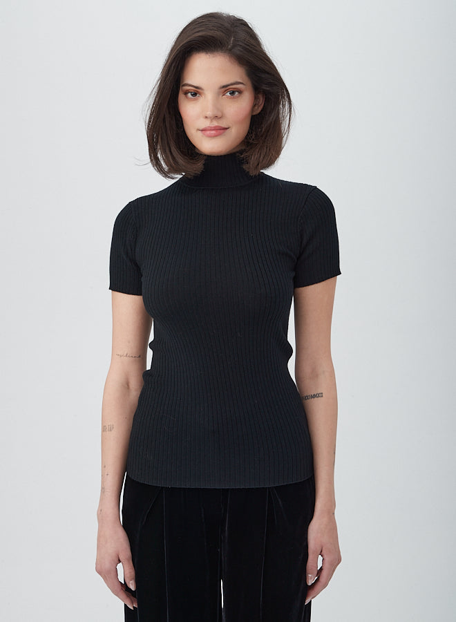 A woman with straight, shoulder-length brown hair wears the Armeni Merino Wool Short Sleeve Mockneck Top and stands against a plain light background, looking at the camera with a slight smile.