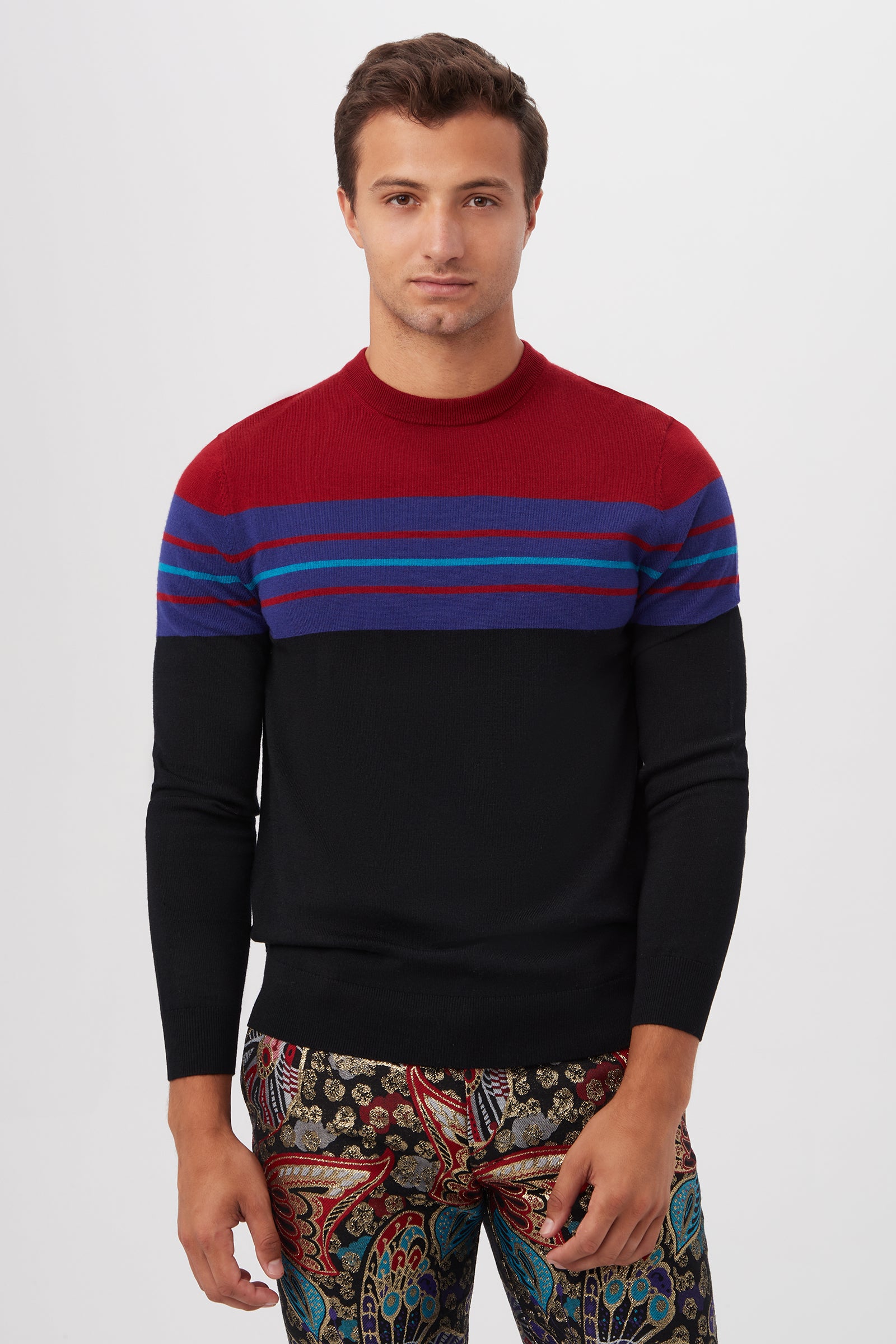 A man faces forward, wearing the Romero Crewneck Sweater in Black MLT, styled with patterned paisley and floral pants against a plain white background.