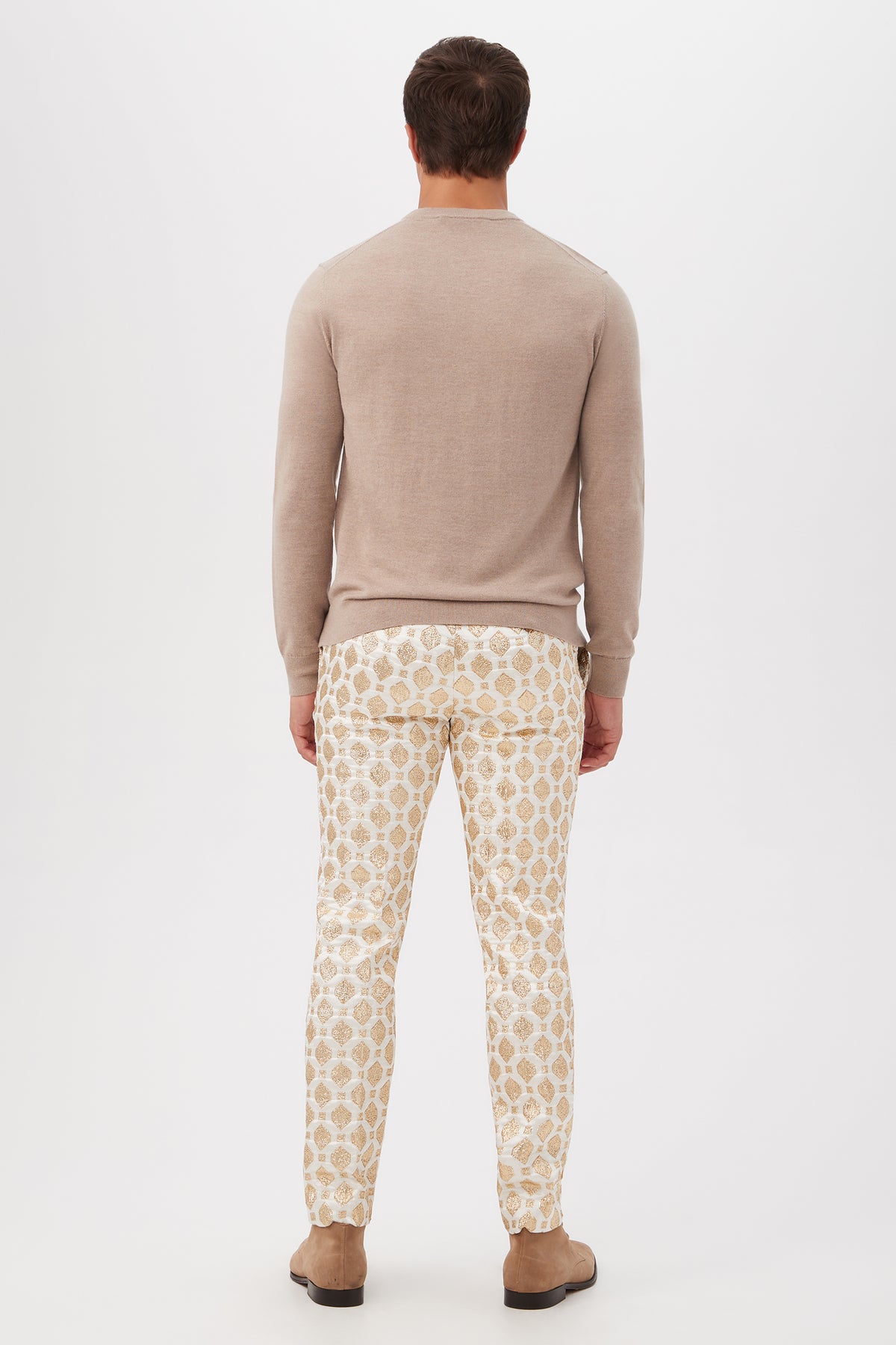 A man faces away against a plain white background, wearing the Weston Airedale Terrier Sweater in light beige merino wool, paired with patterned white and beige pants and tan shoes.