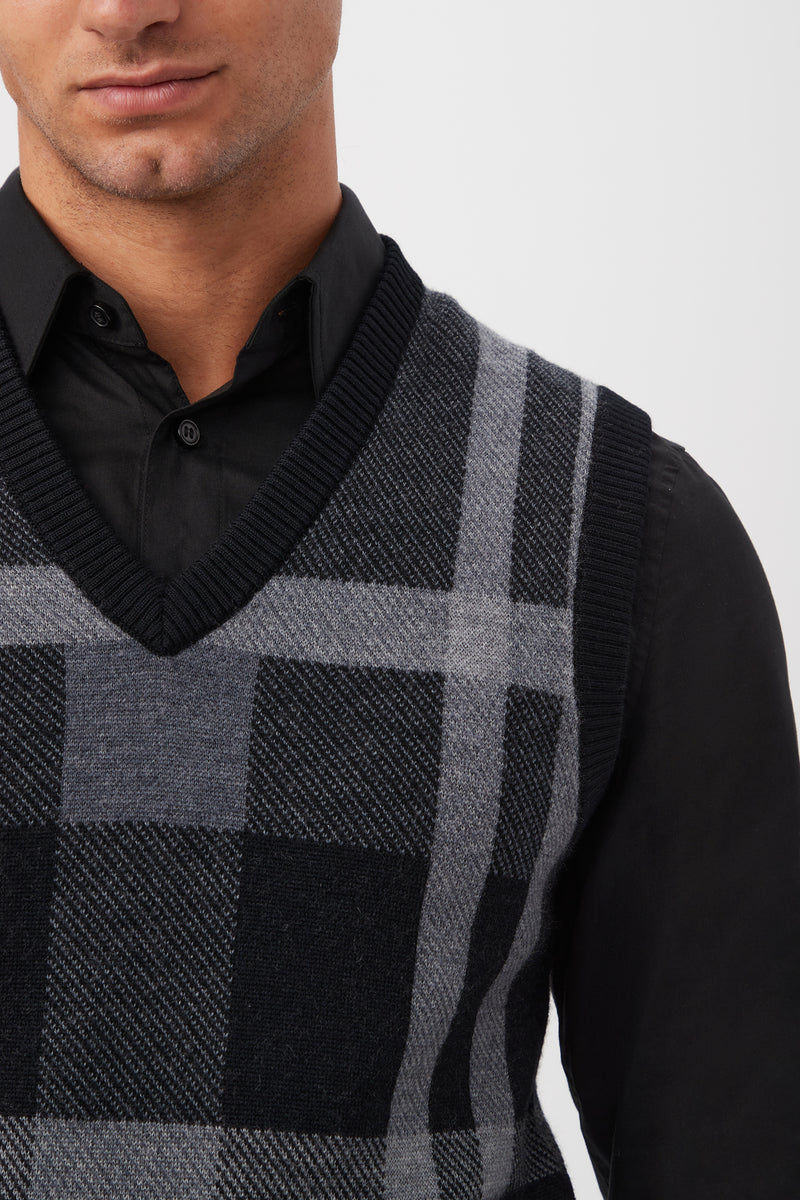A person wearing the Neso Plaid Knit Sweater Vest - Merino Wool in gray and black over a black collared shirt, shown from shoulders to mid-chest against a plain background.
