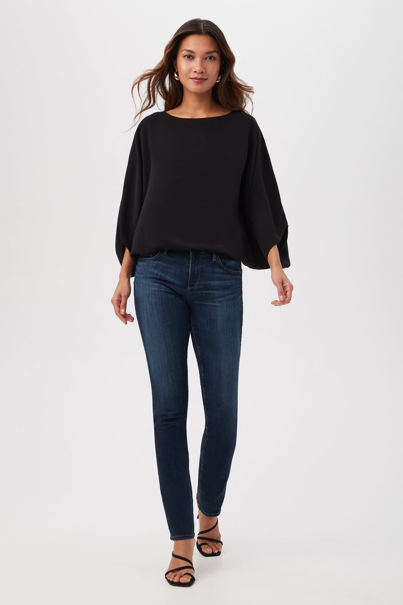 A woman walks confidently in the Manhattan Relaxed Short Dolman Sleeve Top, dark blue skinny jeans, and black sandals against a plain white background.
