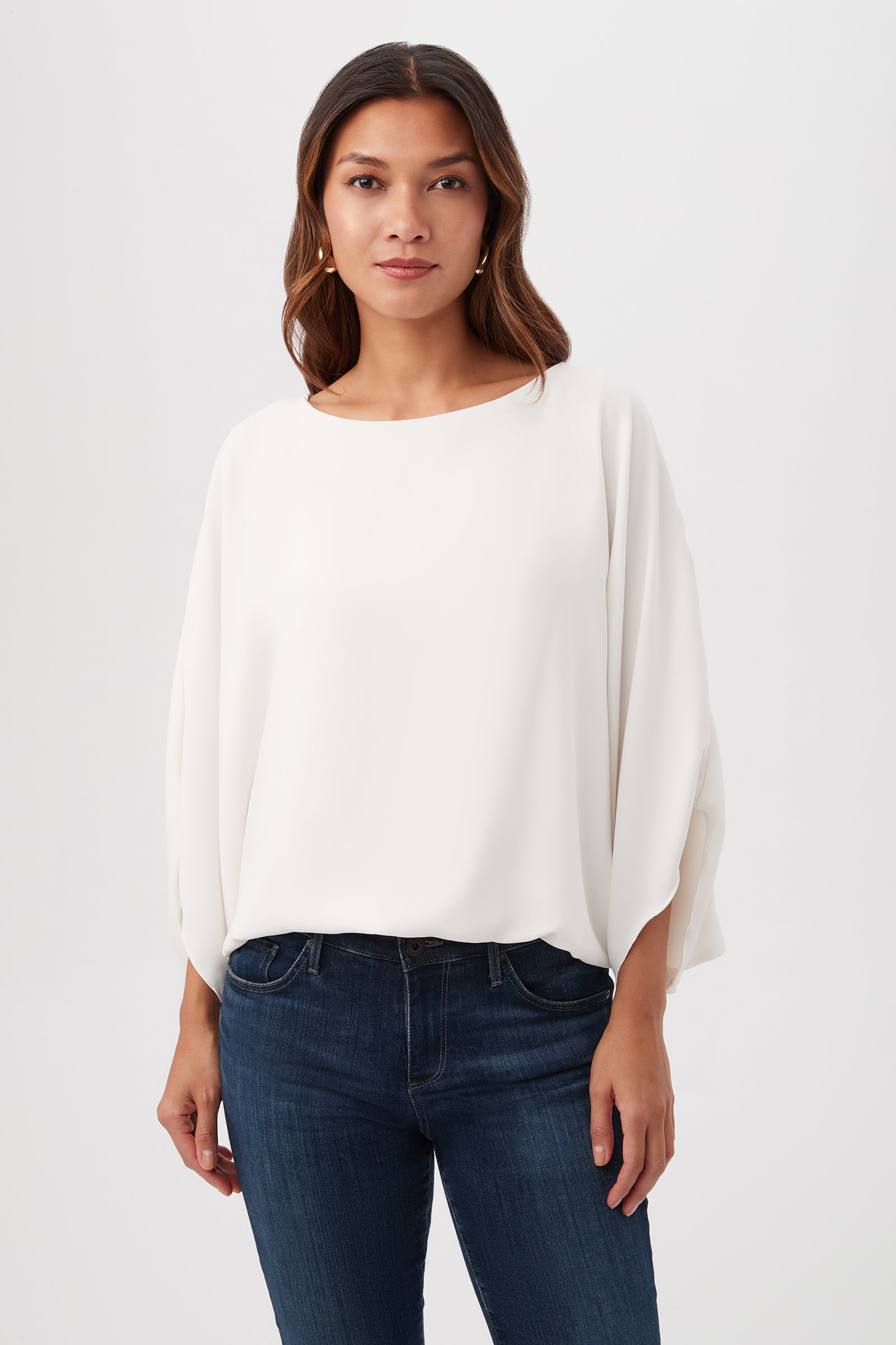 A woman stands against a plain background, wearing the Manhattan Relaxed Short Dolman Sleeve Top in Winter White with blue jeans, looking directly at the camera with a neutral expression.