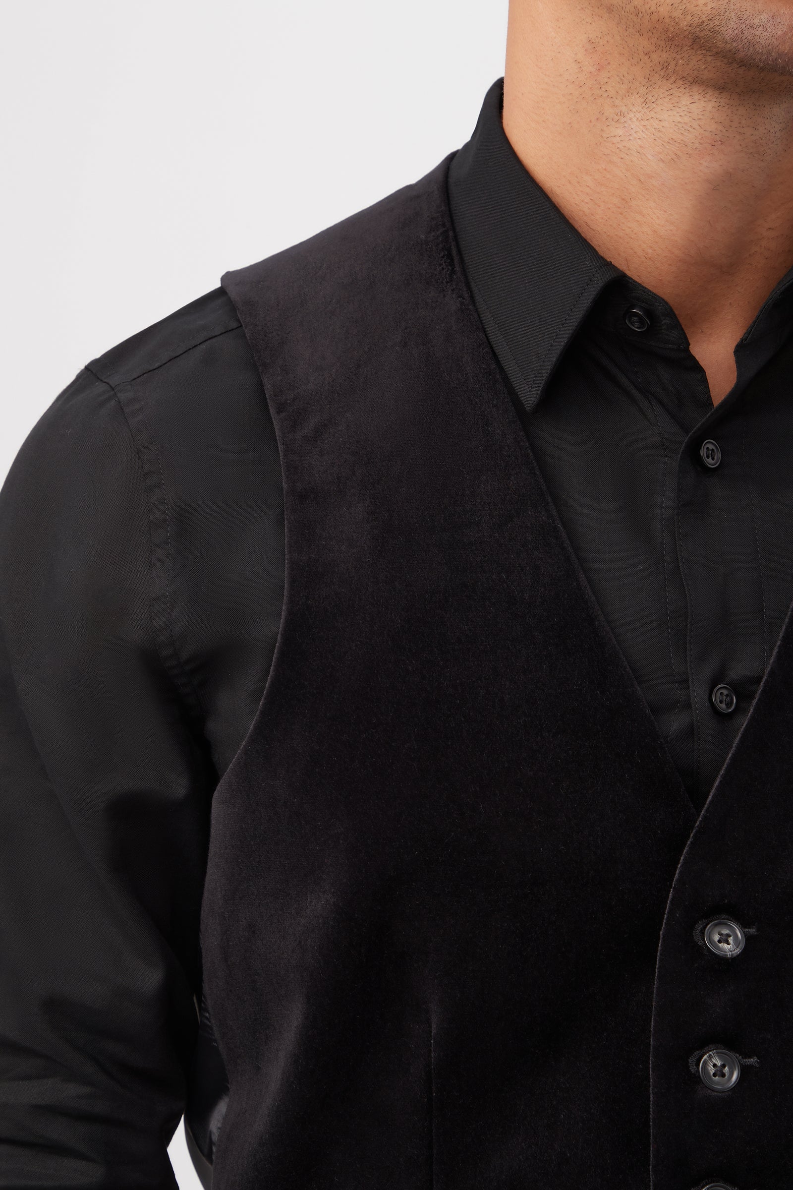 A person wearing the Irving Vest - Black Velveteen over a black dress shirt, shown from shoulders to just above the waist with part of the face cropped, showcases this formal look against a plain light background.