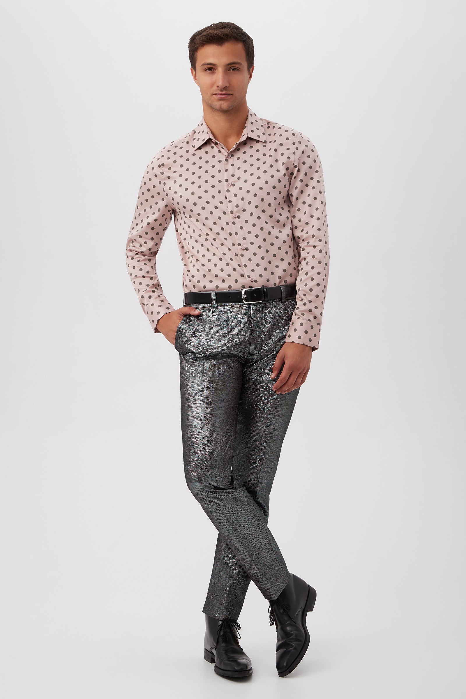 A man with short brown hair strikes a confident pose against a white background wearing the Aaron Slim Fit Long-Sleeve Shirt in light pink polka dots, metallic silver pants, a black belt, and black dress shoes.