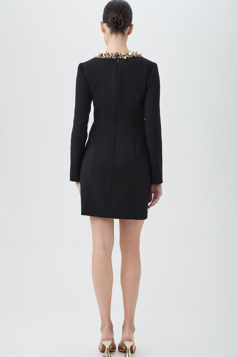 A woman wearing the Darliah Black Long-Sleeve Cocktail Dress with gold trim.