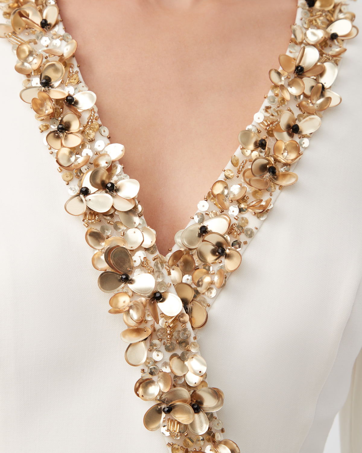 Close-up of the Darliah Long-Sleeve Cocktail Dress With Gold Trim, featuring a white V-neckline adorned with gold and pearl floral embellishments and small beads along the edge.