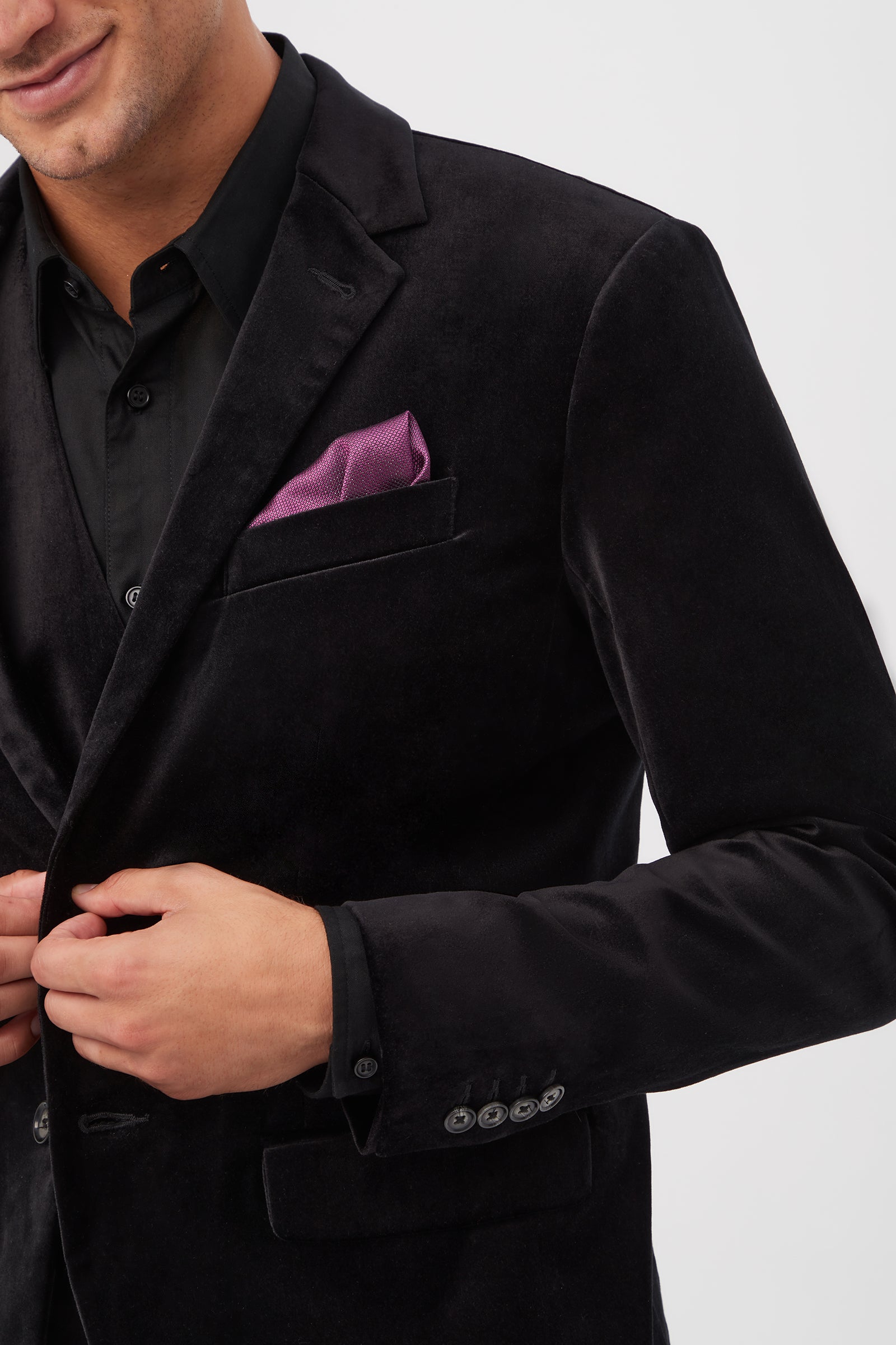 A person adjusts the Thurston Blazer - Black Velveteen over a black shirt, with a purple pocket square visible in the chest pocket, against a plain white background.