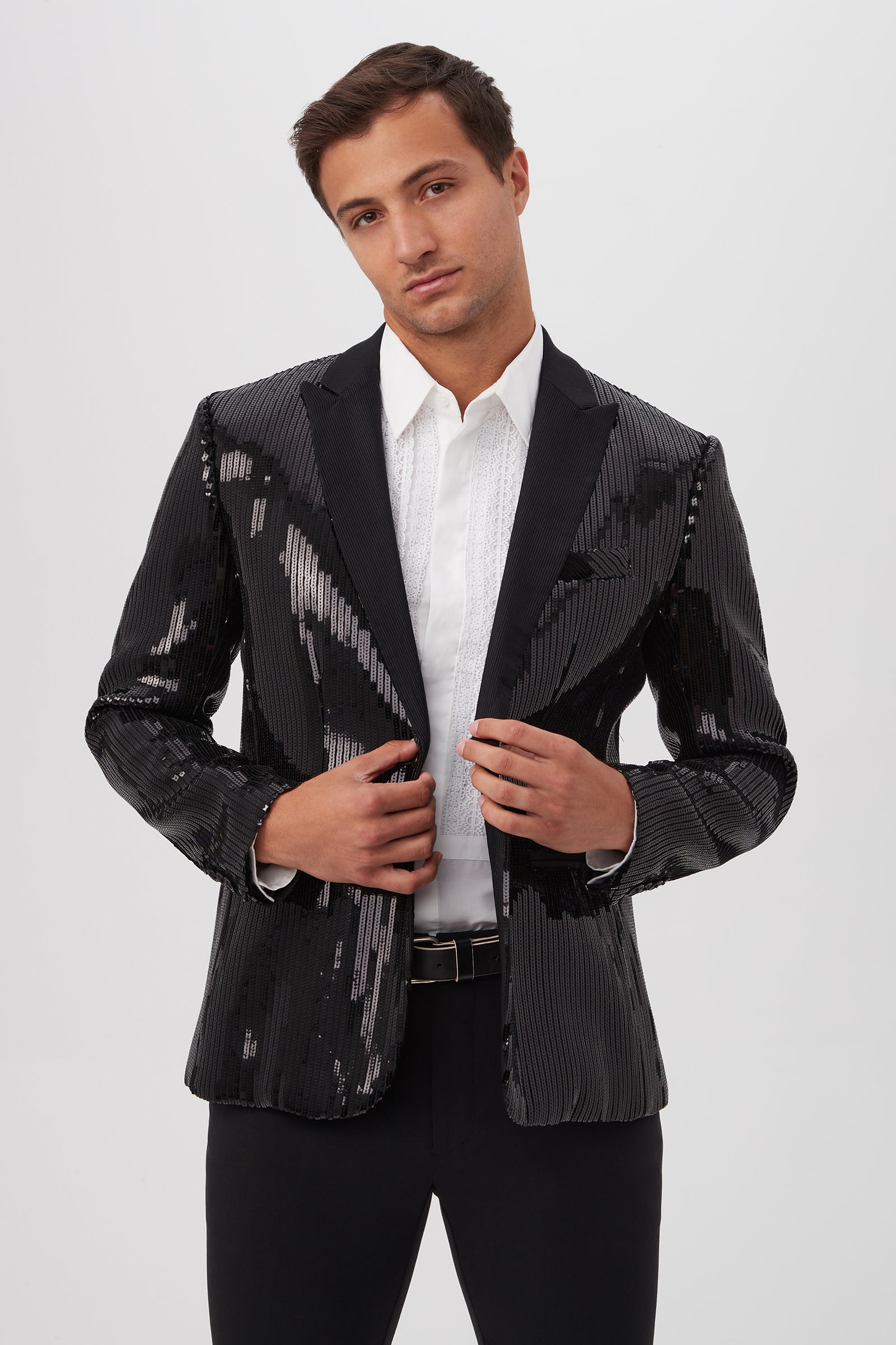 A man wears the Coleman Blazer - Stripe Sequin in black over a white dress shirt with black pants, standing confidently against a plain white background.