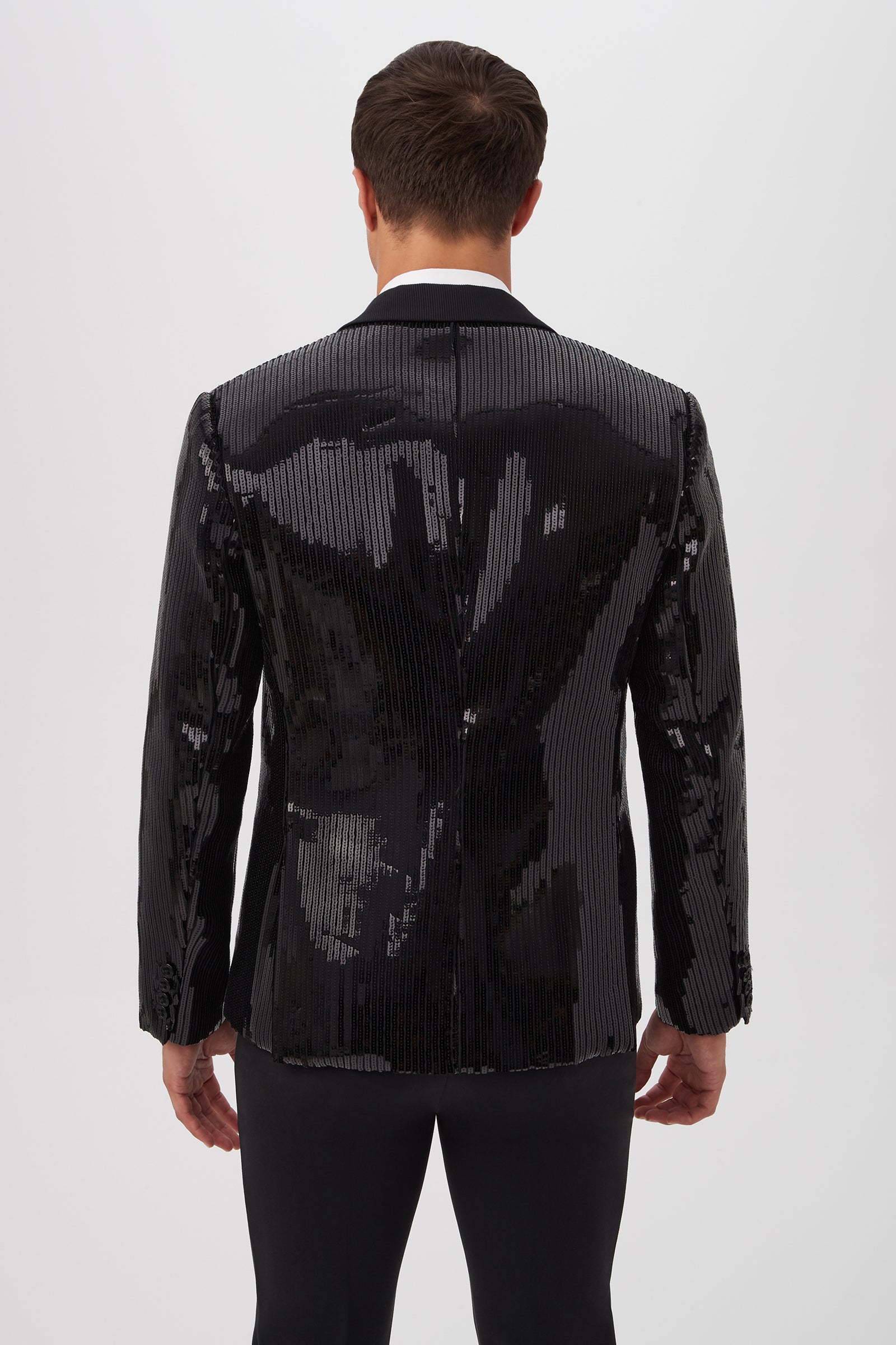 A man faces away from the camera, wearing the Coleman Blazer - Stripe Sequin with vertical black sequins and black pants, set against a plain white background.