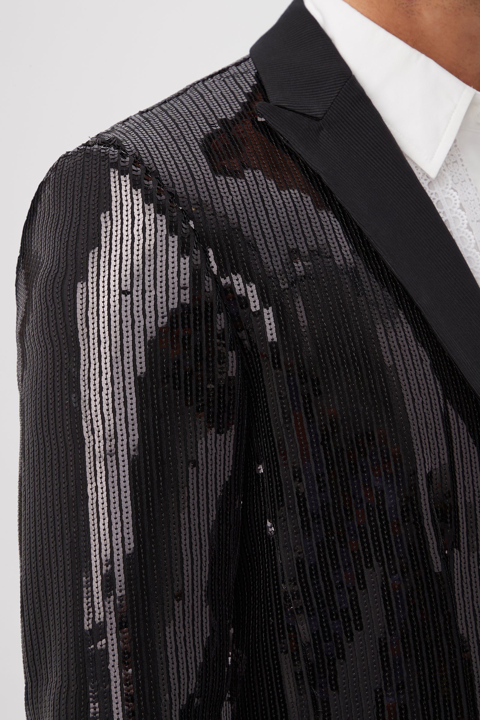 Close-up of a person wearing the Coleman Blazer - Stripe Sequin, featuring black sequins in vertical stripes over a white dress shirt. Only the shoulder and part of the chest are visible, highlighting the blazers shiny, textured effect.