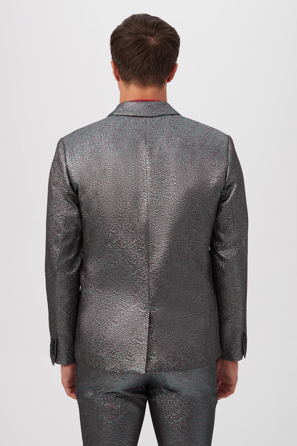 A person stands facing away from the camera wearing the Thurston Blazer in Mini Stained Glass Jacquard, a shiny, textured silver suit, against a plain white background.