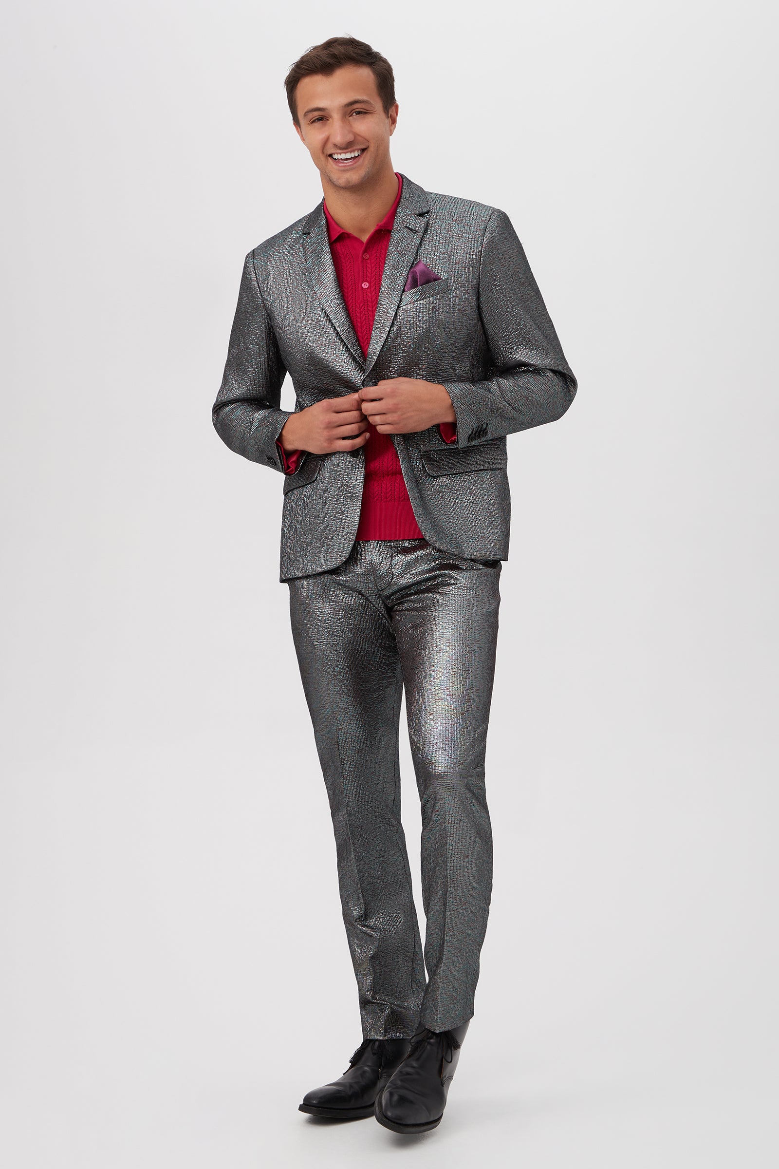 A smiling man stands against a plain background, confidently buttoning the Thurston Blazer in Mini Stained Glass Jacquard. He pairs it with a red dress shirt, black shoes, and a purple pocket square, looking sharp for the camera.
