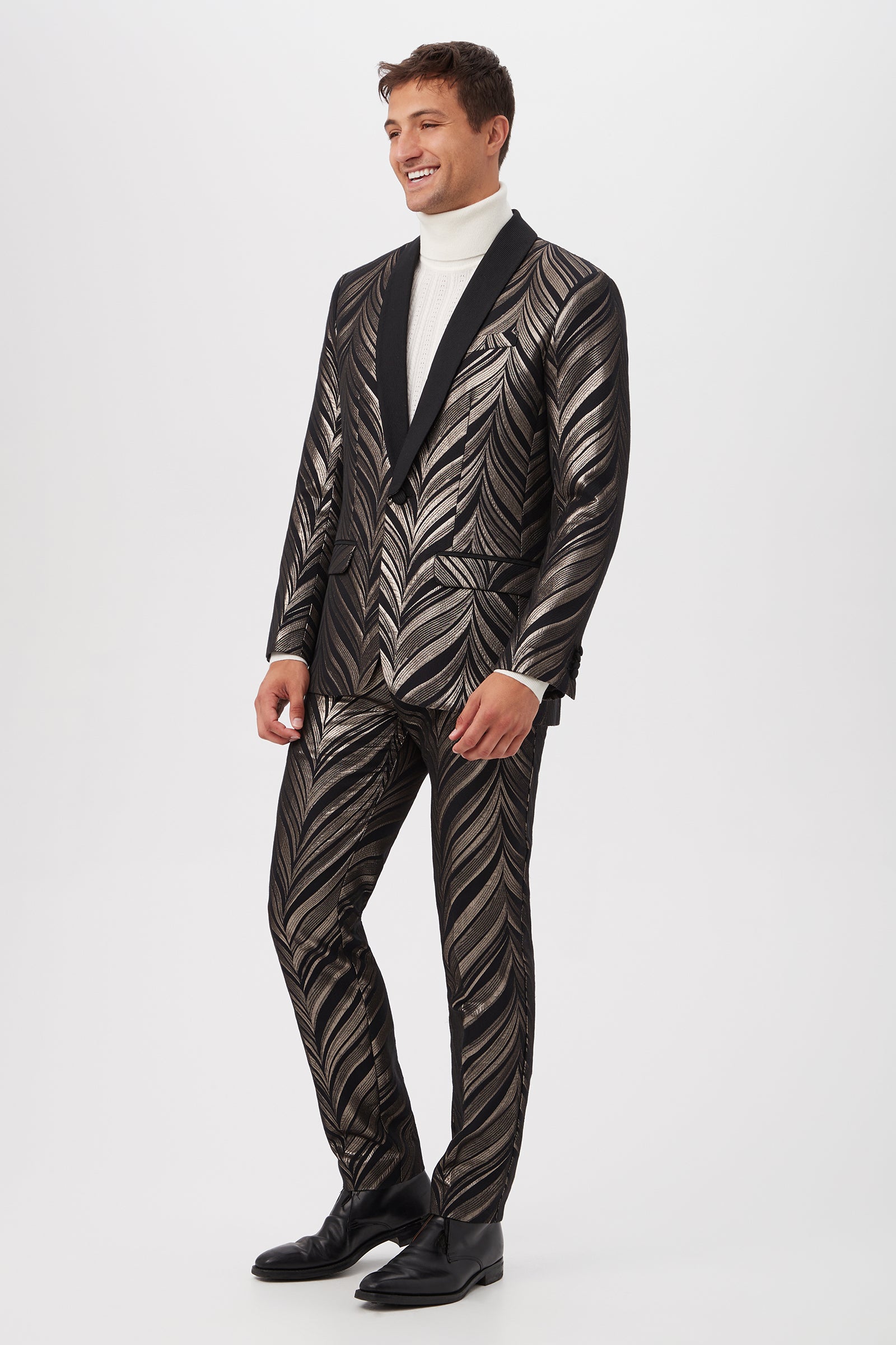 A man smiles while wearing the Alfred Blazer - Descanso Chevron Jacquard, paired with a white turtleneck and black dress shoes, posing against a plain white background.