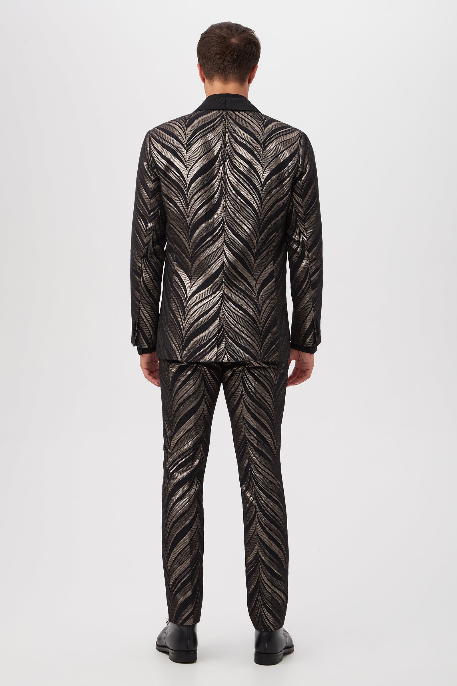 A man, seen from behind, wears the Alfred Blazer in Descanso Chevron Jacquard—a shiny black suit with a silver chevron pattern—paired with black shoes, standing against a plain white background.