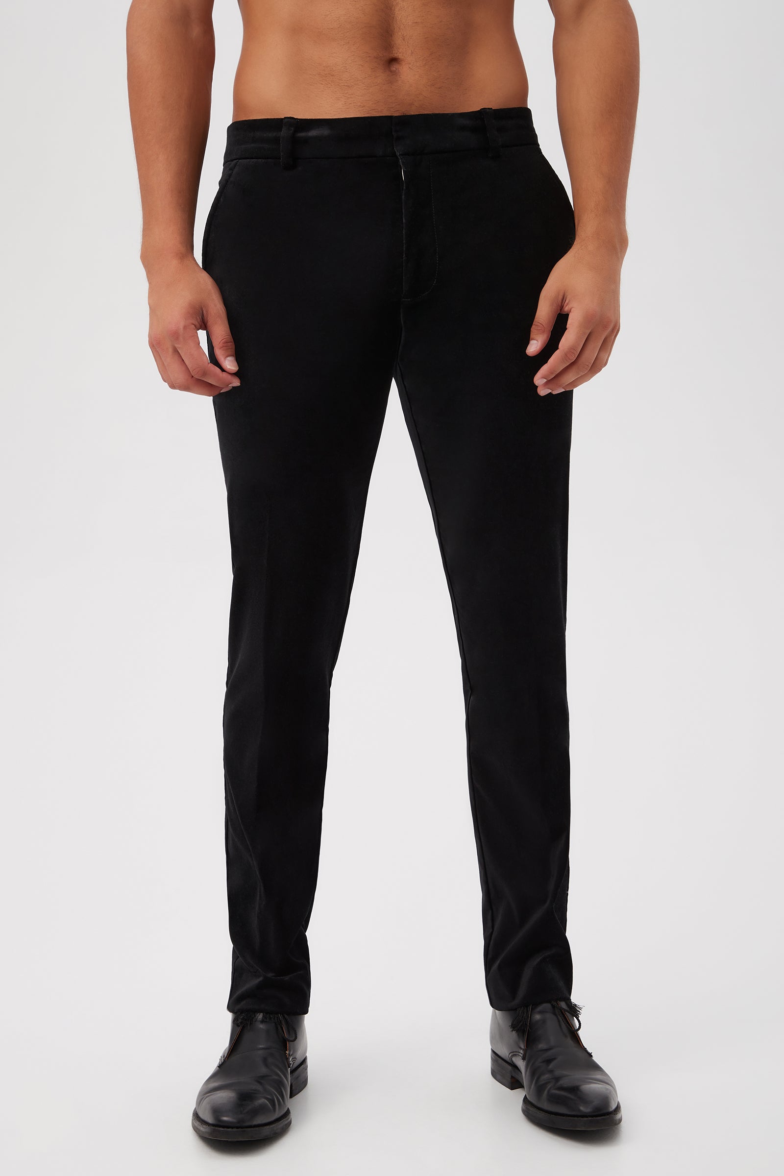 A man wears the Clyde Slim Trouser in black velveteen with black dress shoes. The photo is cropped from the shoulders down, set against a plain light background.