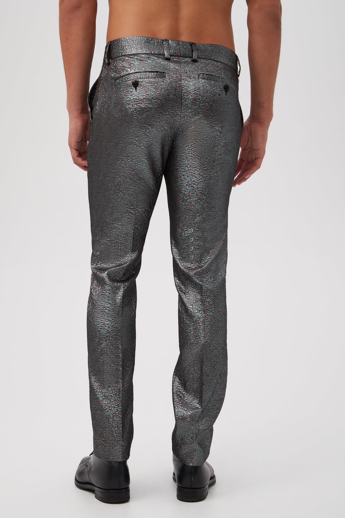 A shirtless man faces away, wearing Clyde Slim Trouser - Stained Glass Jacquard in shiny, textured silver and black dress shoes against a plain white background.