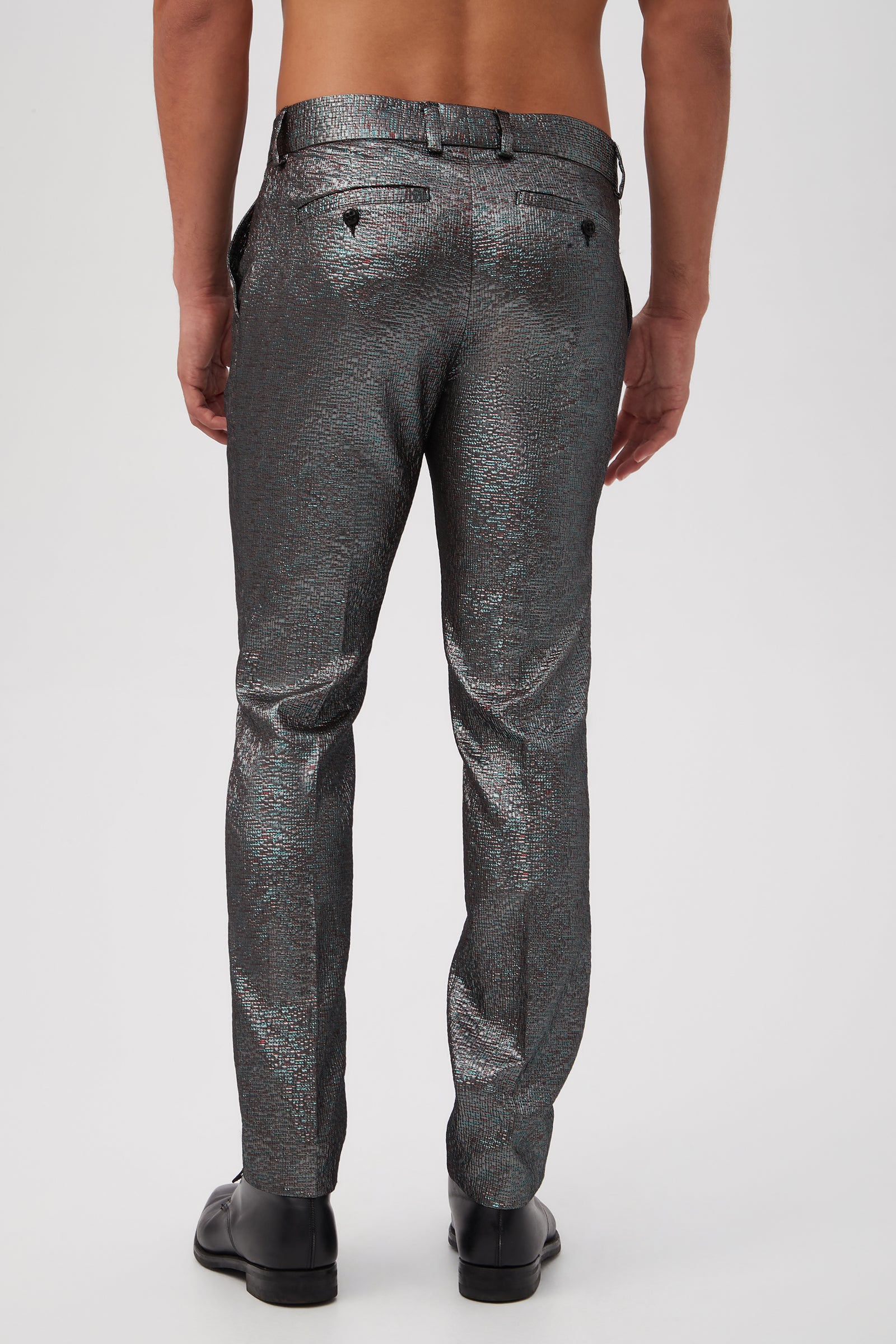 A shirtless man faces away, wearing Clyde Slim Trouser - Stained Glass Jacquard in shiny, textured silver and black dress shoes against a plain white background.