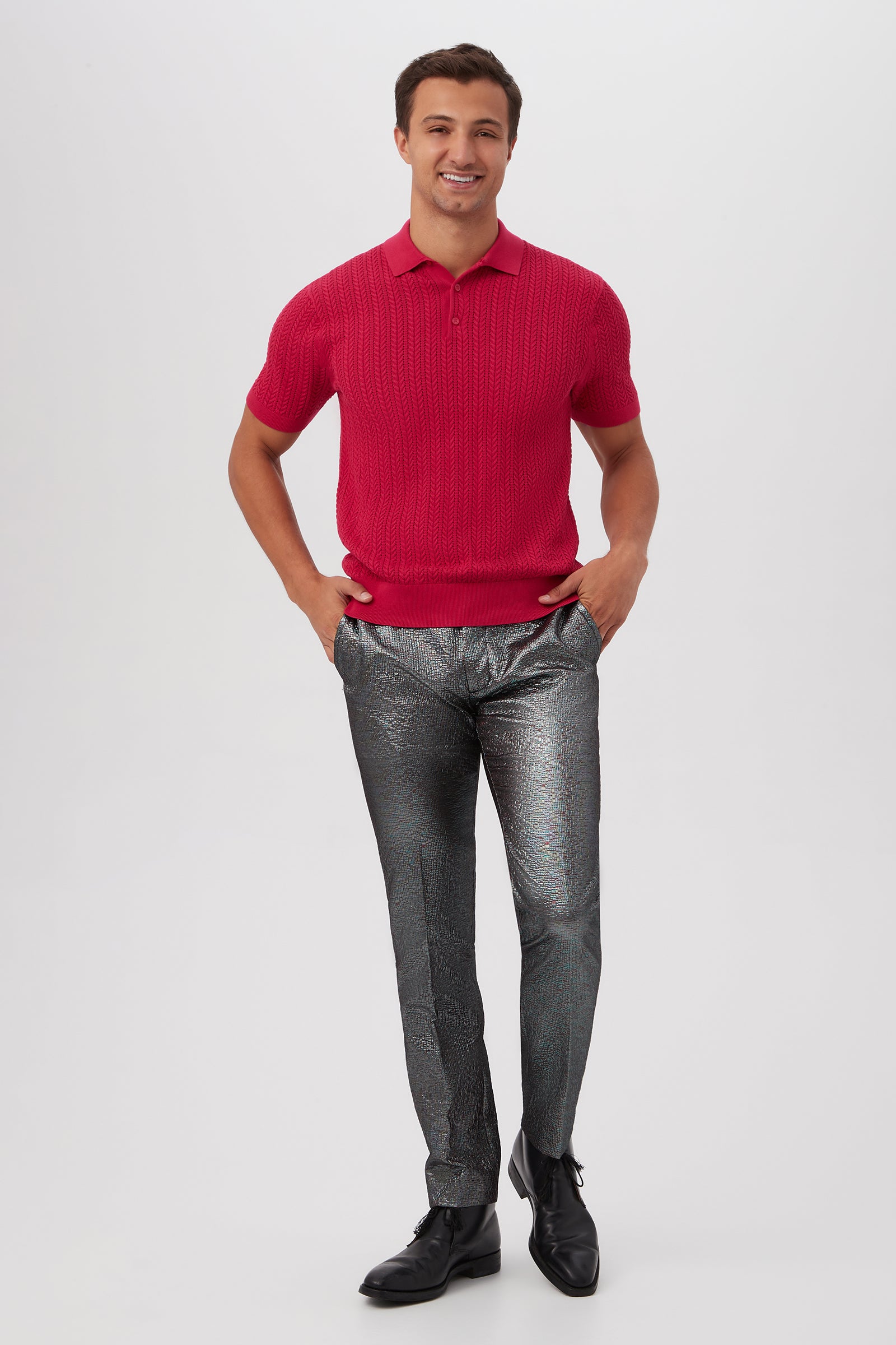 A man stands smiling with hands in pockets, wearing the Maxton Short-Sleeve Polo - Cotton Modal in red, shiny silver metallic pants, and black dress shoes against a plain white background.