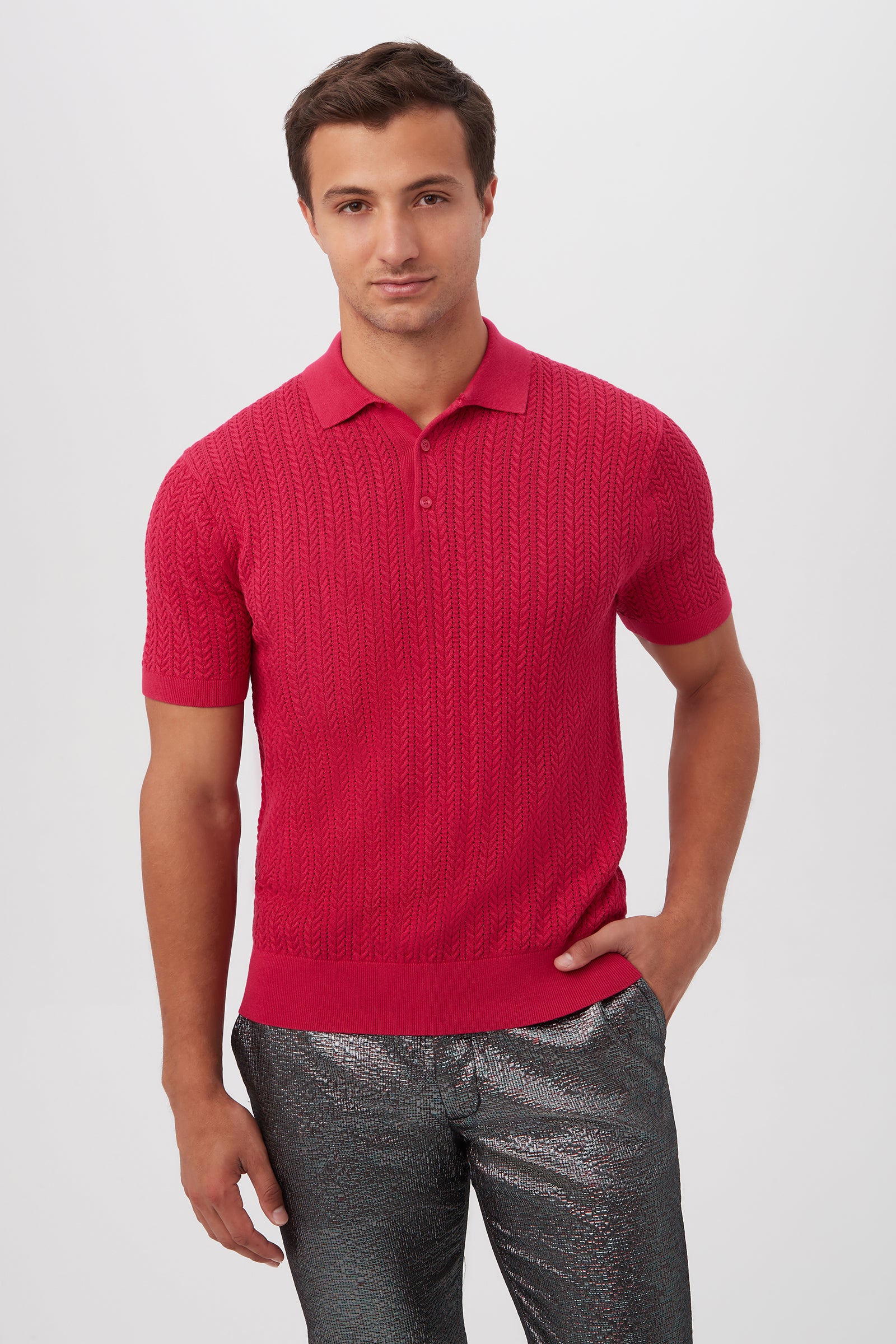 A man with a neutral expression poses against a plain background, wearing the Maxton Short-Sleeve Polo in Fairy Fuchsia and shiny silver pants, one hand on his hip.