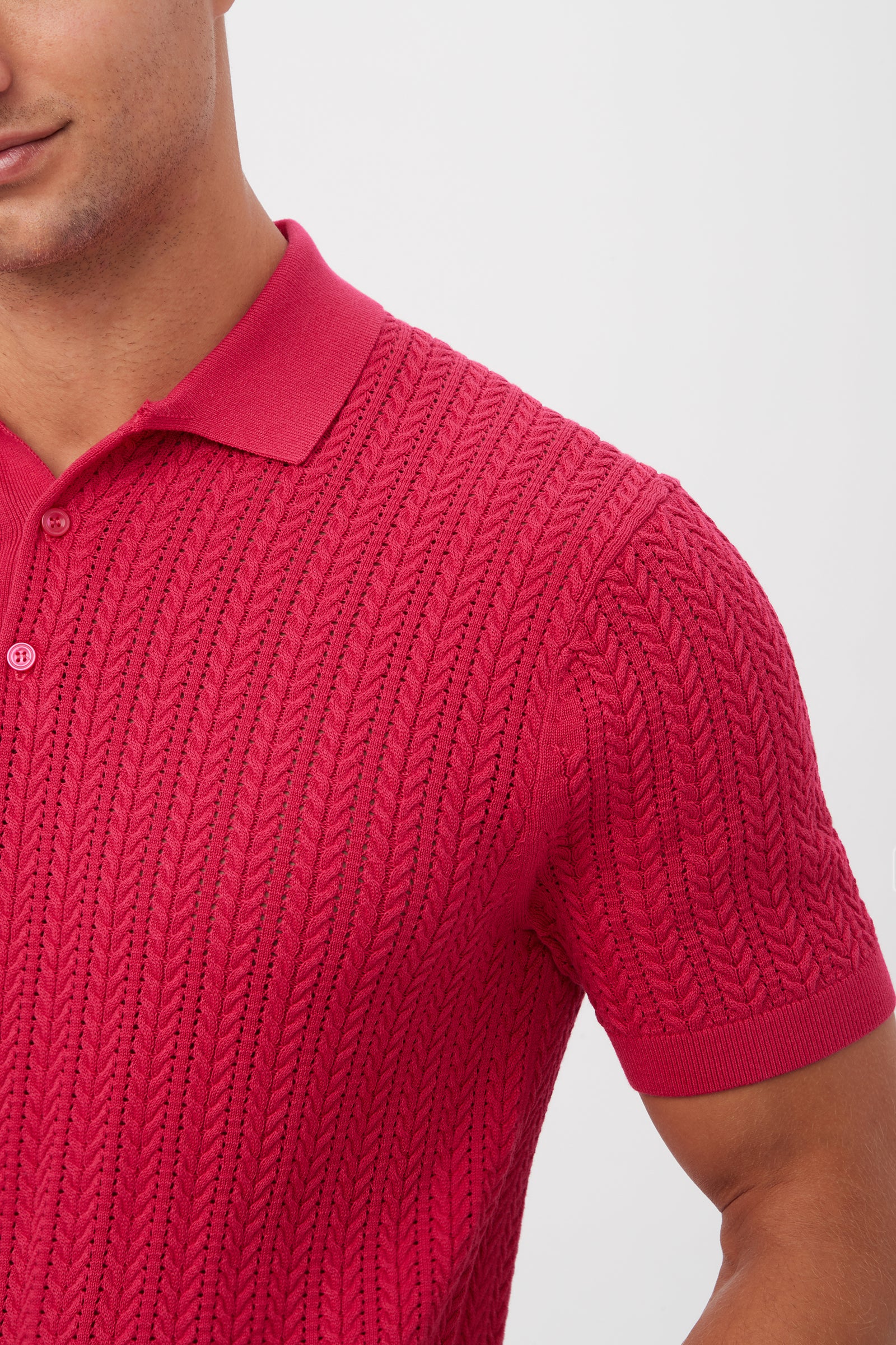 A man models the Maxton Short-Sleeve Polo - Cotton Modal in bright red, featuring a cable-knit texture, collar, and buttons. Only his lower face and upper torso are shown.