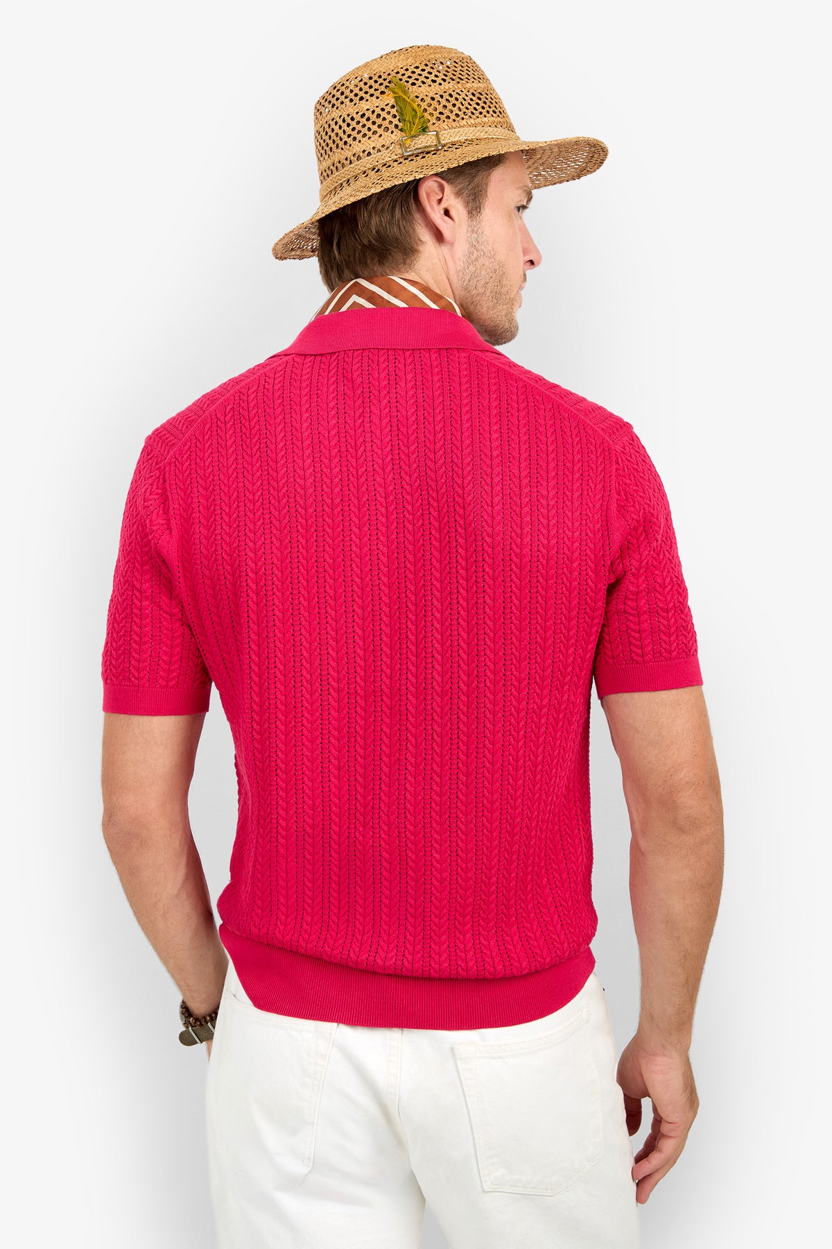 A man wearing a straw hat with a green feather, the Maxton Short-Sleeve Polo - Cotton Modal in red, and white pants stands facing away against a plain white background.