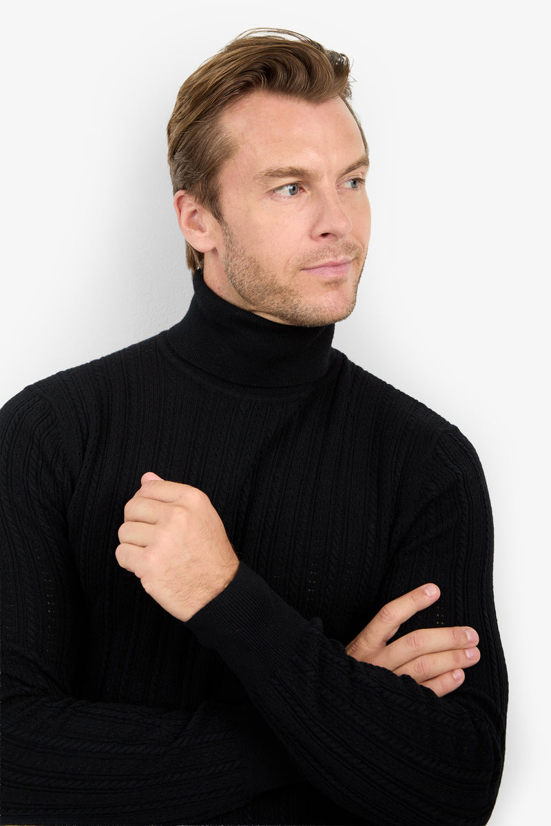 A man with short light brown hair wears the Oberon Turtleneck Sweater - Merino Wool in black, standing with arms crossed and a neutral expression against a plain white background.