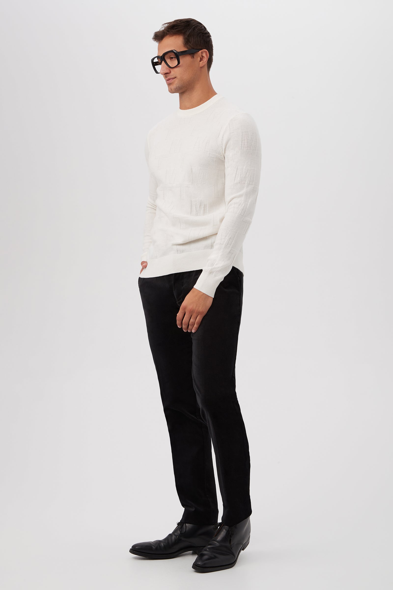 A man wearing black glasses, black pants, black shoes, and the Mr Turk Crewneck Sweater - Merino Wool stands against a plain white background with one hand in his pocket.