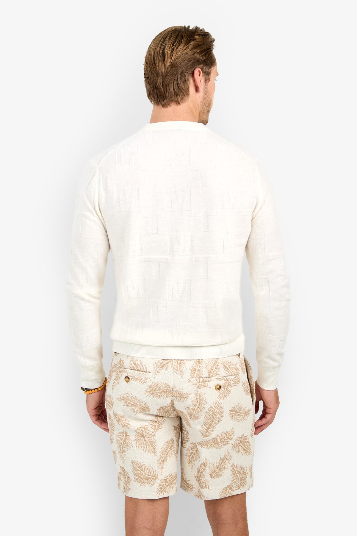 A man with light brown hair, seen from behind, wears the Mr Turk Crewneck Sweater - Merino Wool and beige leaf-patterned shorts against a plain white background.