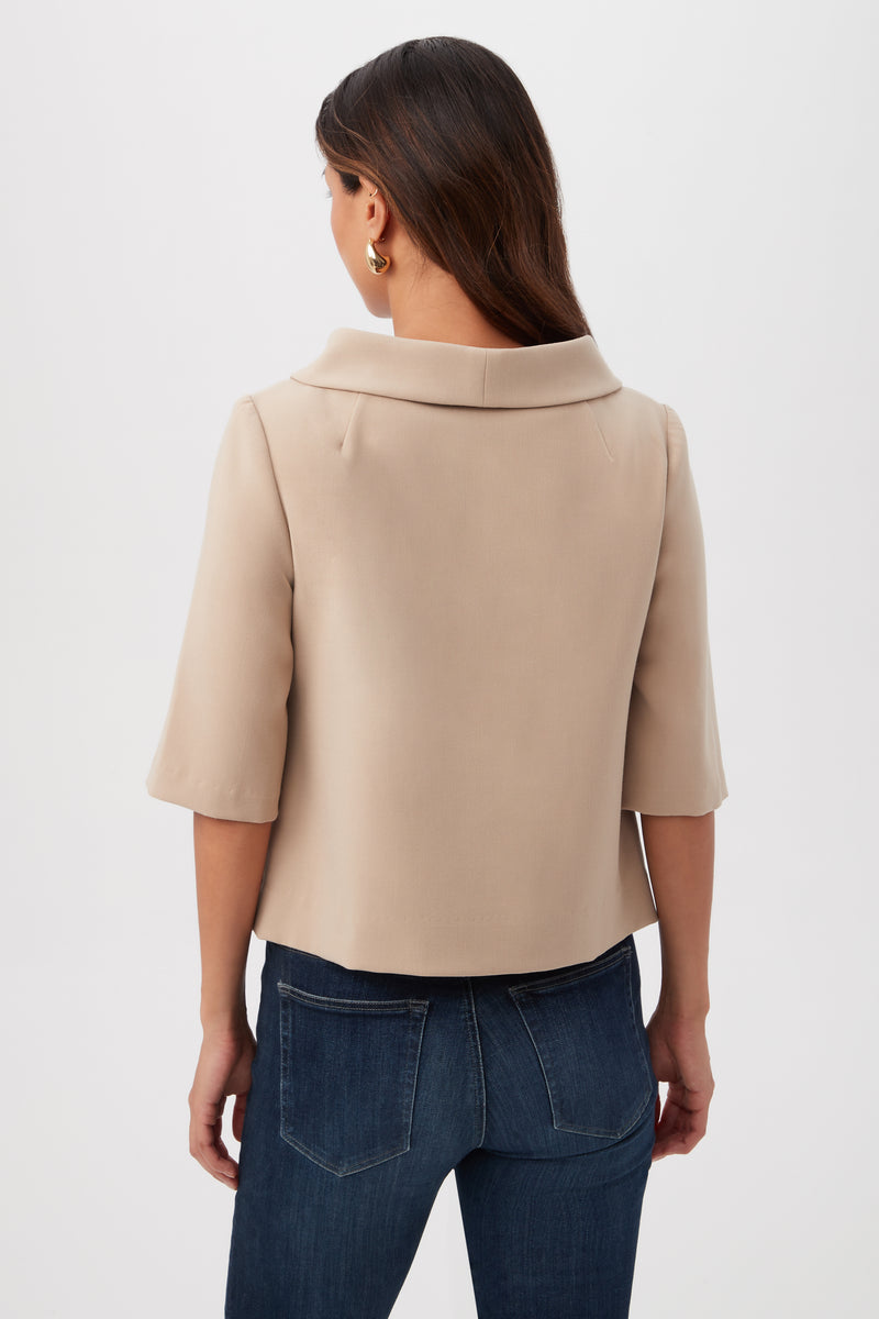 A woman with long brown hair is seen from the back wearing the Kailee Short-Sleeve Folded Collar Top in beige and dark blue jeans, against a plain white background.