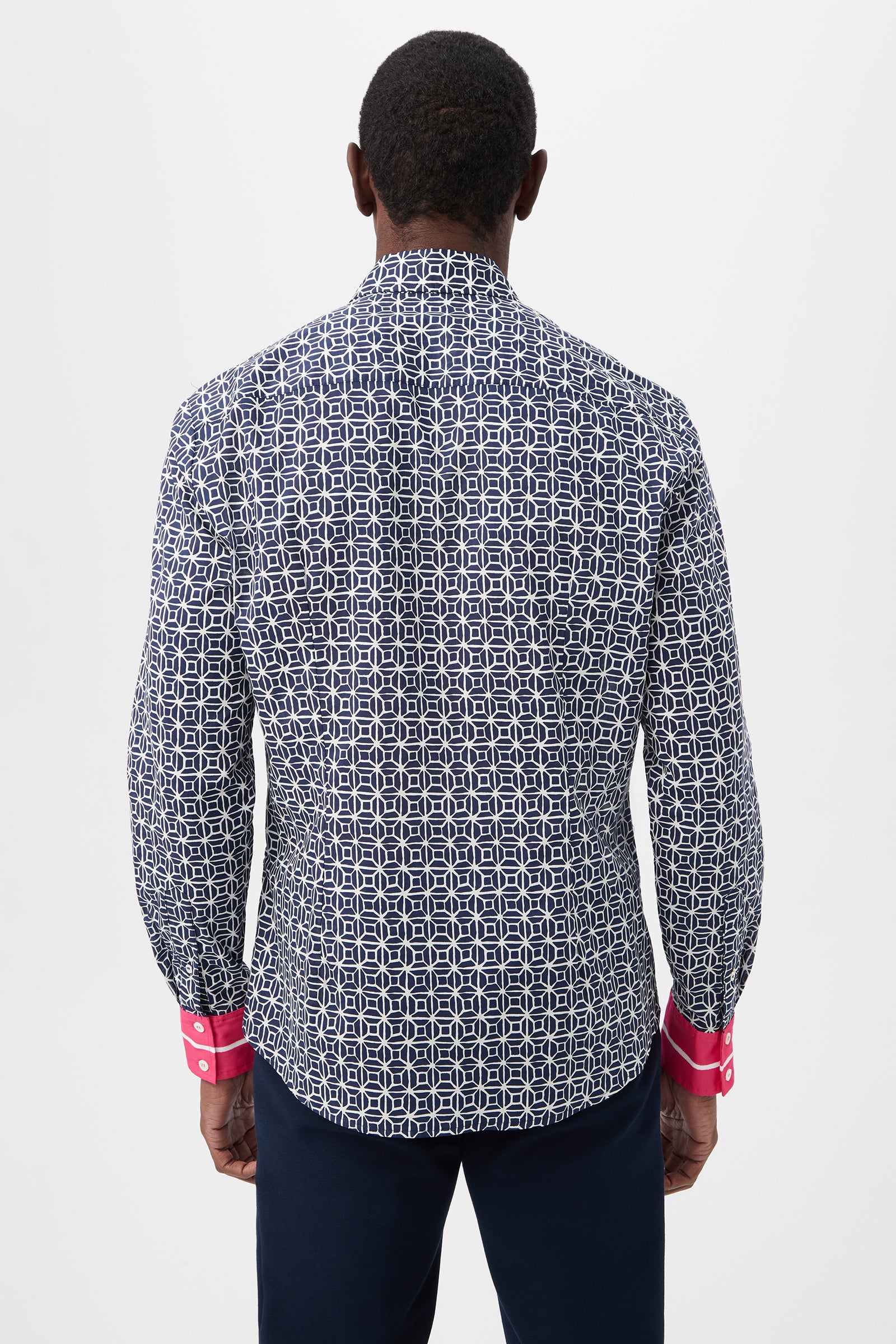 A man stands facing away, wearing the Aaron 2 Slim Long-Sleeve Shirt in navy blue and white with bright pink cuffs and dark pants, set against a plain white background.