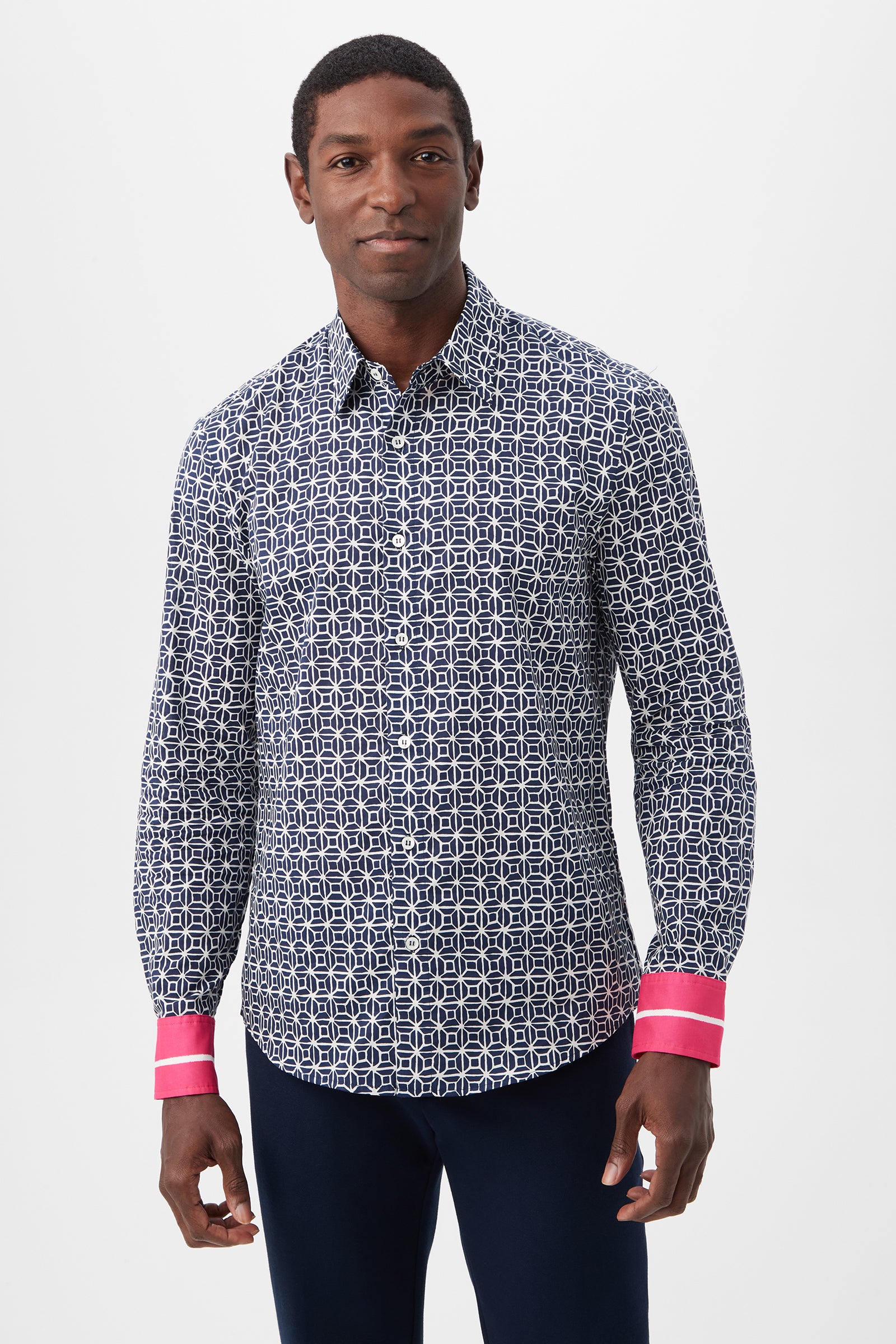 A man wears the Aaron 2 Slim Long-Sleeve Shirt in Indigo Multi, featuring a geometric pattern and bright pink cuffs, as he stands smiling against a plain white background.
