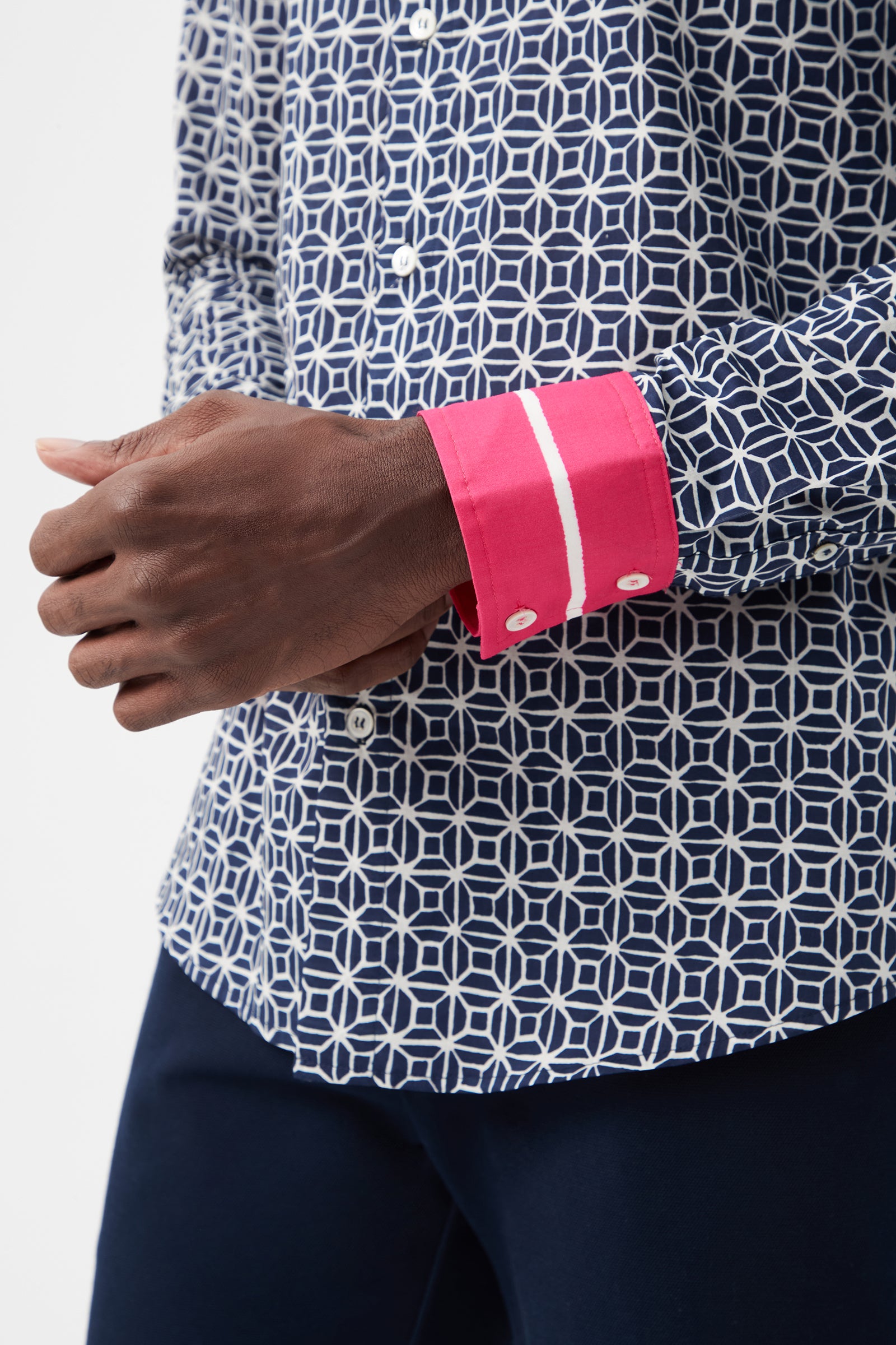 Wearing the Aaron 2 Slim Long-Sleeve Shirt in navy blue with a geometric pattern and bright pink cuffs, a person shown from the waist up adjusts their cuff while dressed in dark pants.