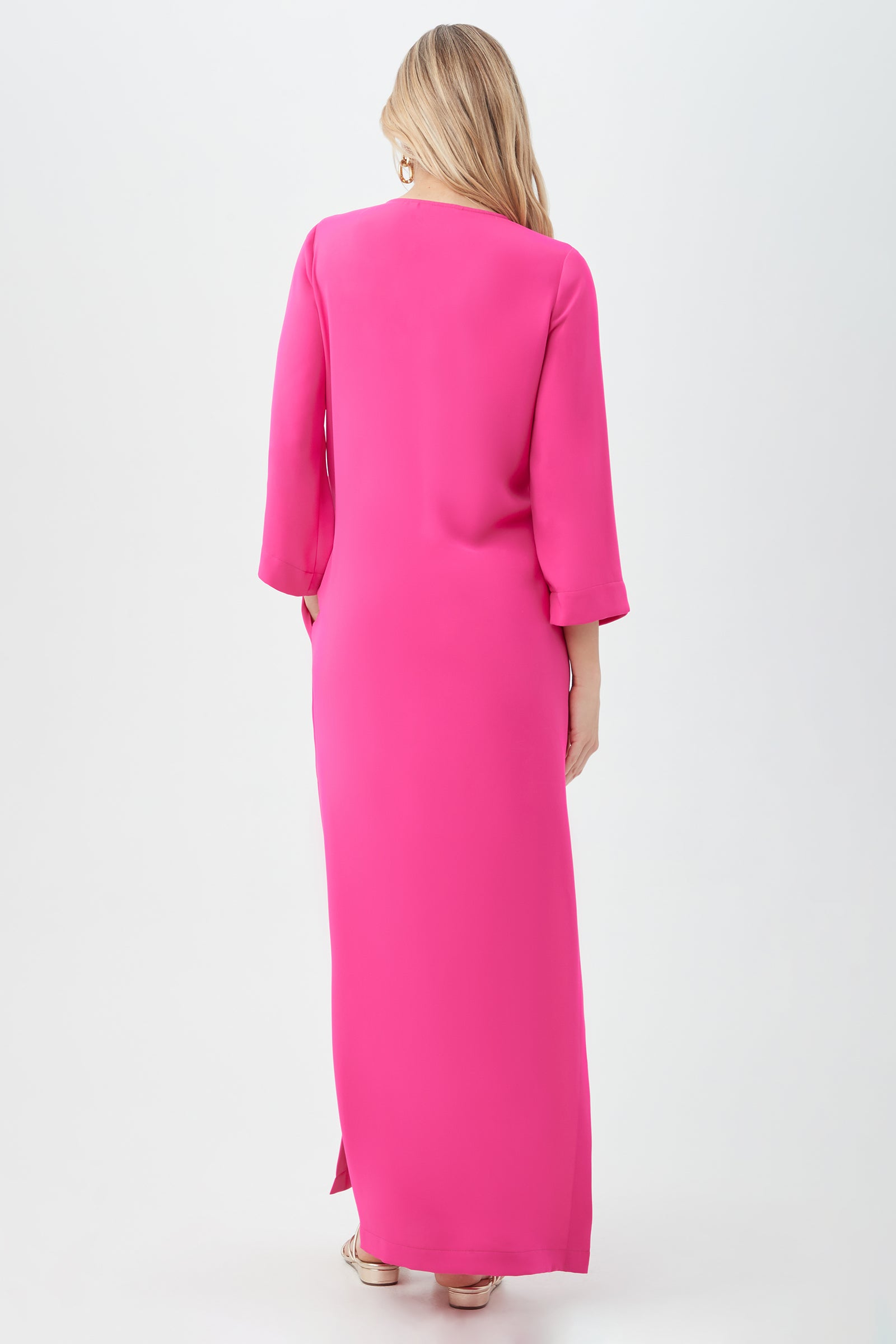 A woman with long blonde hair, seen from behind, wears the Catamaran 3/4-Sleeve Maxi Dress in bright pink and sandals, posed against a plain white background.