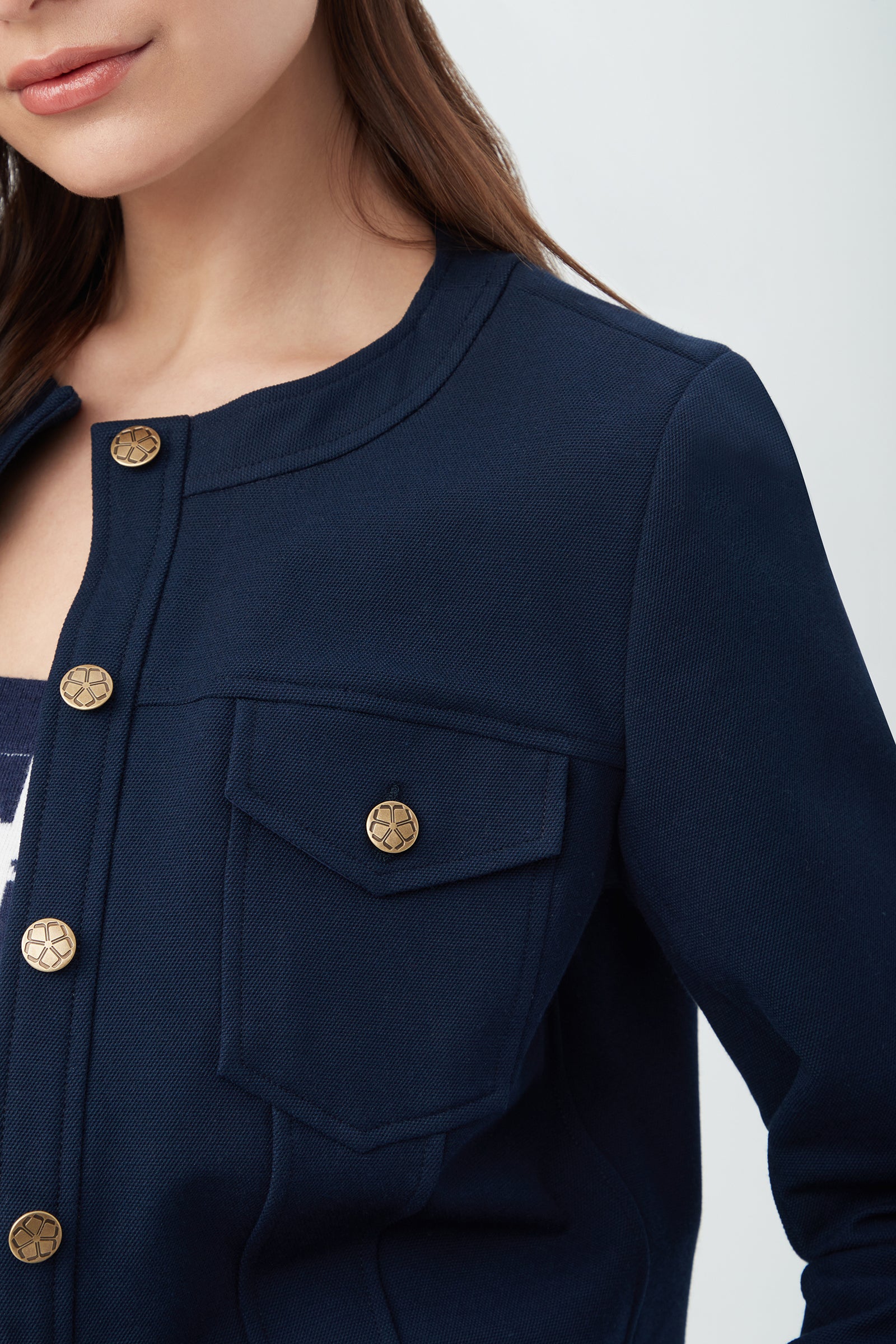A woman models the Gail Jacket—a navy blue piece with gold buttons and a front chest pocket—against a light background, showing only the lower half of her face and upper torso.